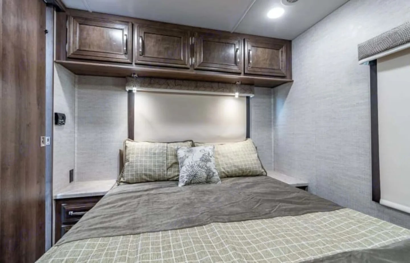 This cozy RV rental bedroom features overhead wood cabinets, a plush bed with patterned bedding, and reading lights, perfect for travel.. Entegra Coach Esteem 2022