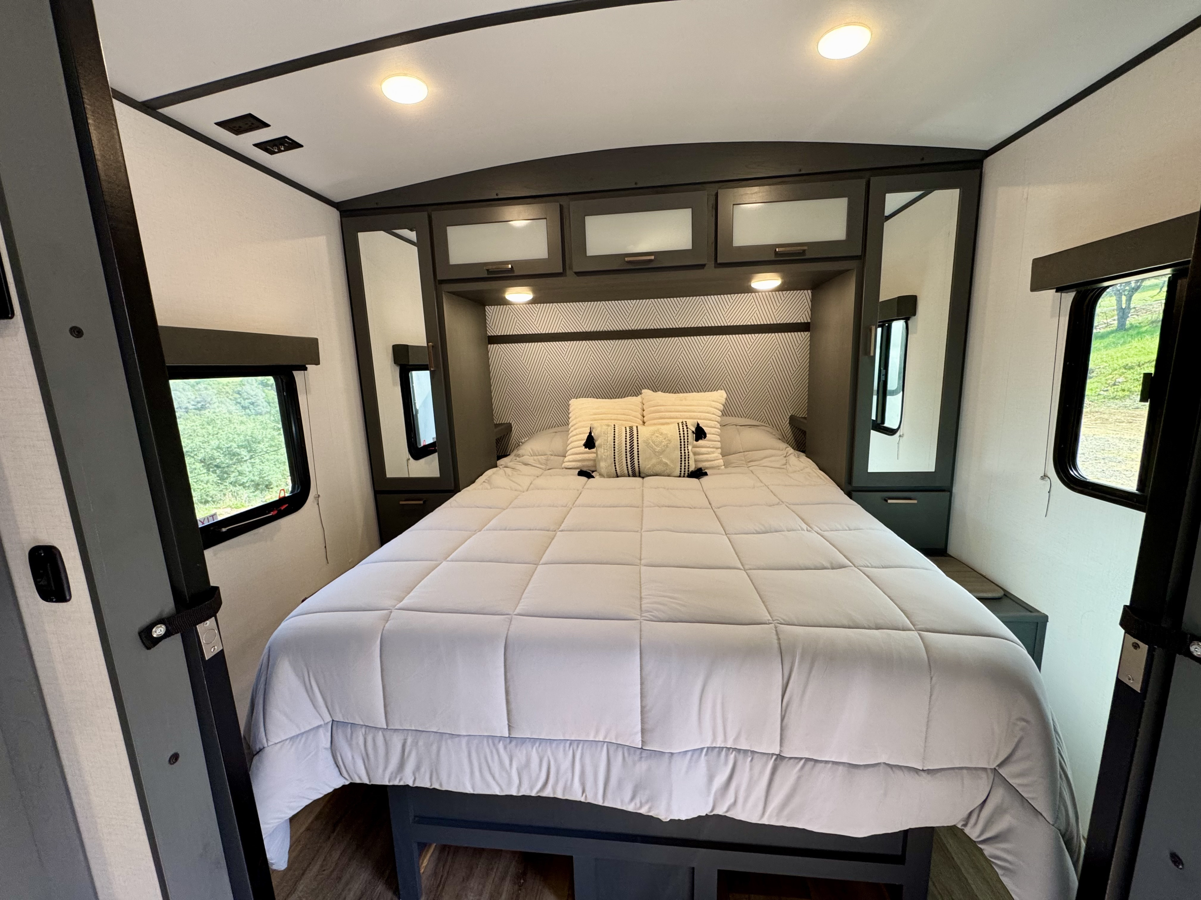 Cozy RV rental bedroom with a comfortable bed, stylish headboard, overhead storage, and dual windows. Ideal for travel trailer stays.. Keystone RV Bullet Ultra Lite 2023