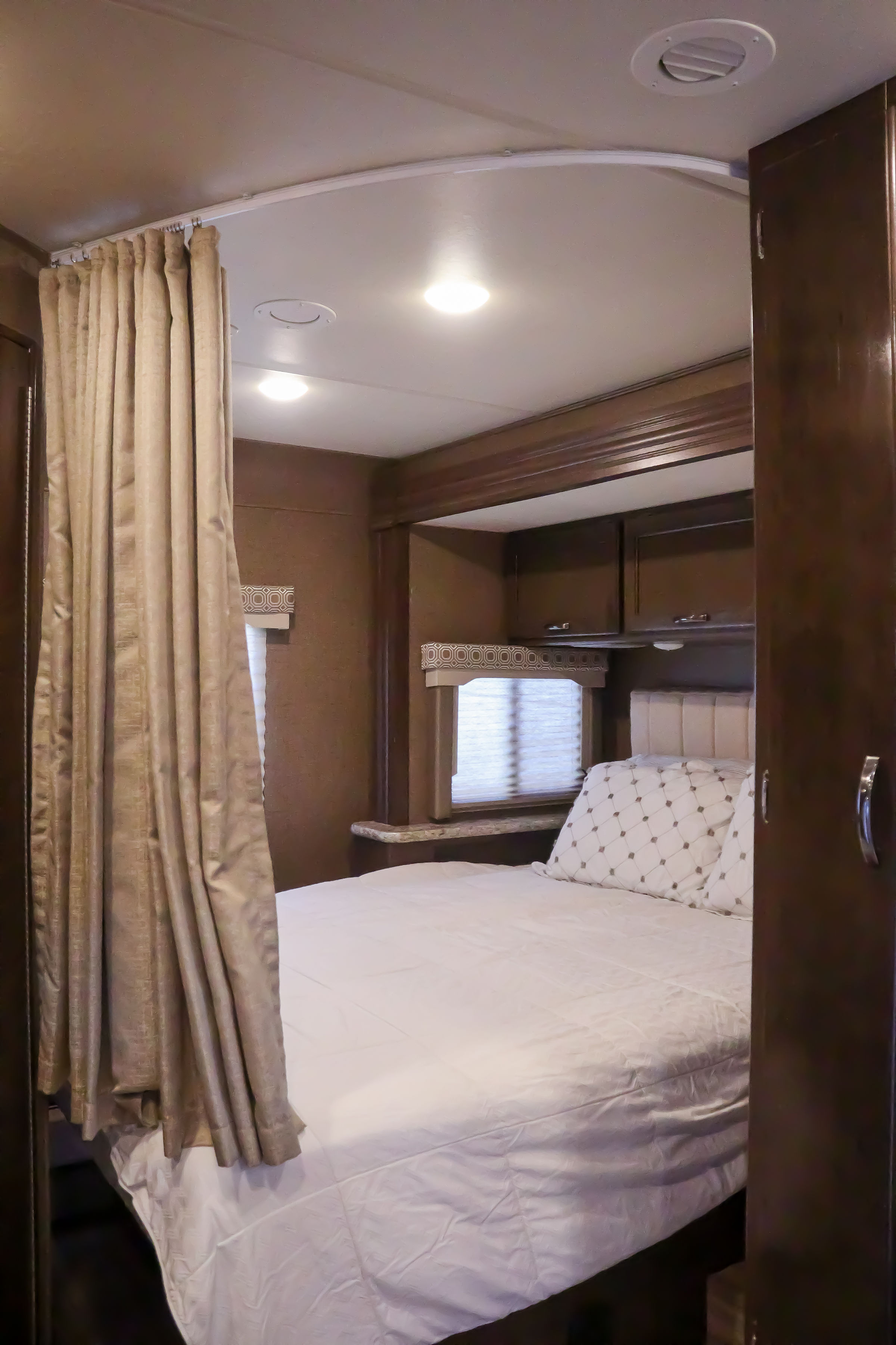 RV rental bedroom with a comfortable bed, a privacy curtain on a curved track, and convenient overhead storage.. Thor Four Winds 2017