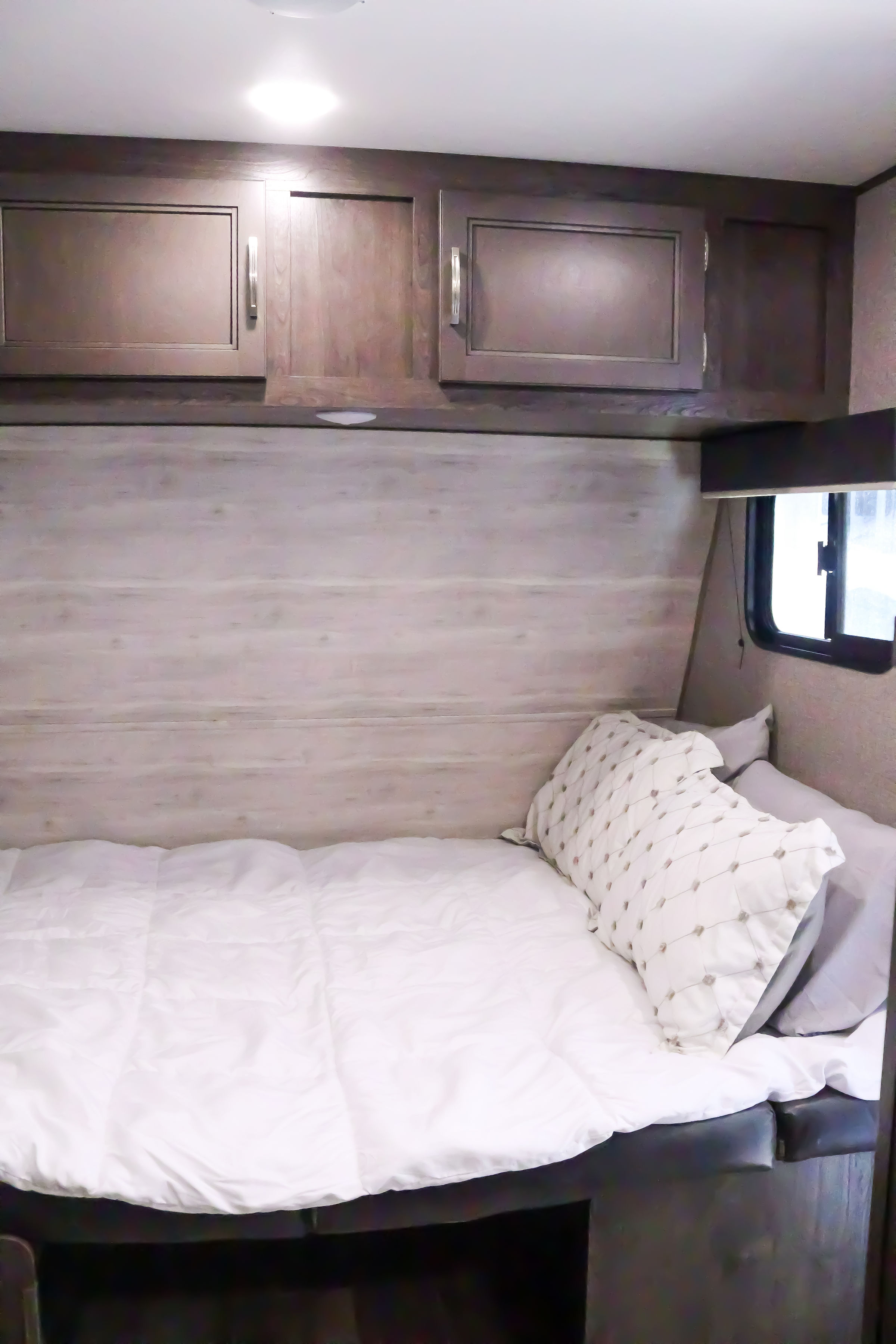 Inviting RV rental bedroom with a neat white bed, decorative pillows, and dark wood cabinets. A compact and cozy sleeping area.. Jayco Baja 2021