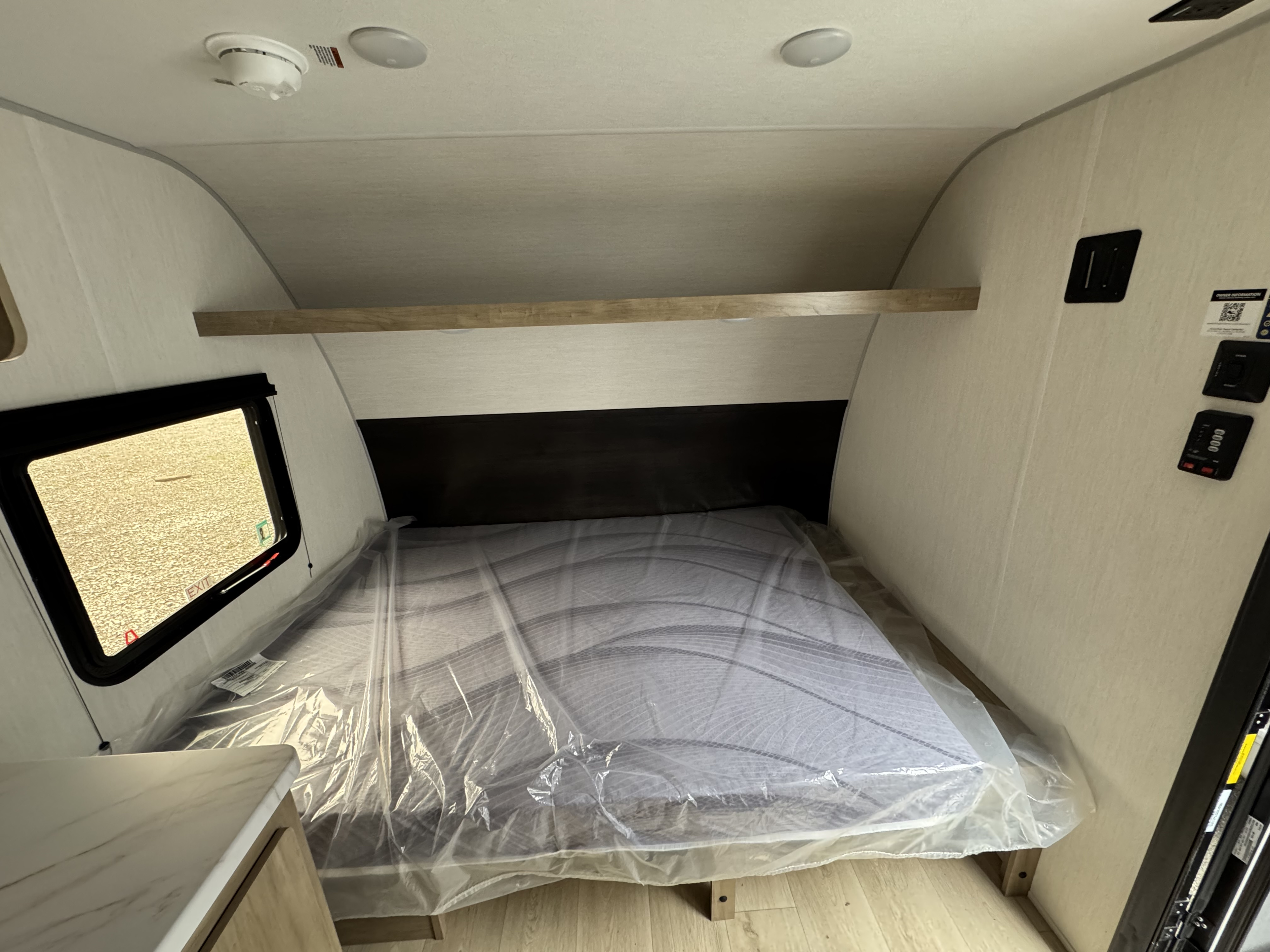 RV rental bedroom interior with a new, plastic-wrapped mattress, overhead shelf, and window, ready for guests.. Forest River WOLF PUP 17LP 2026