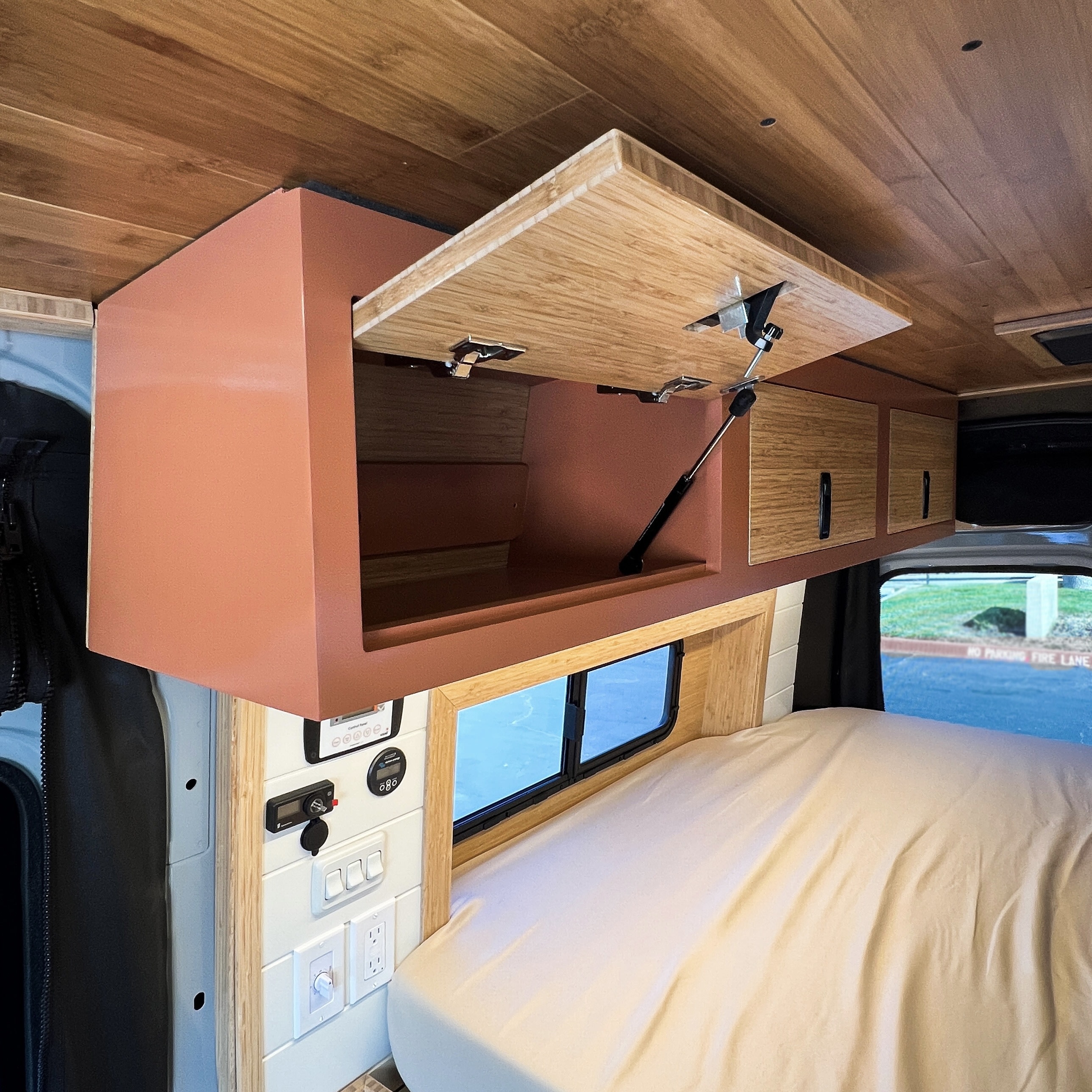 RV rental van's interior: Open bamboo overhead cabinet, coordinating wooden ceiling, cozy bed, and practical control panel system.. Mercedes-Benz Sprinter 2026
