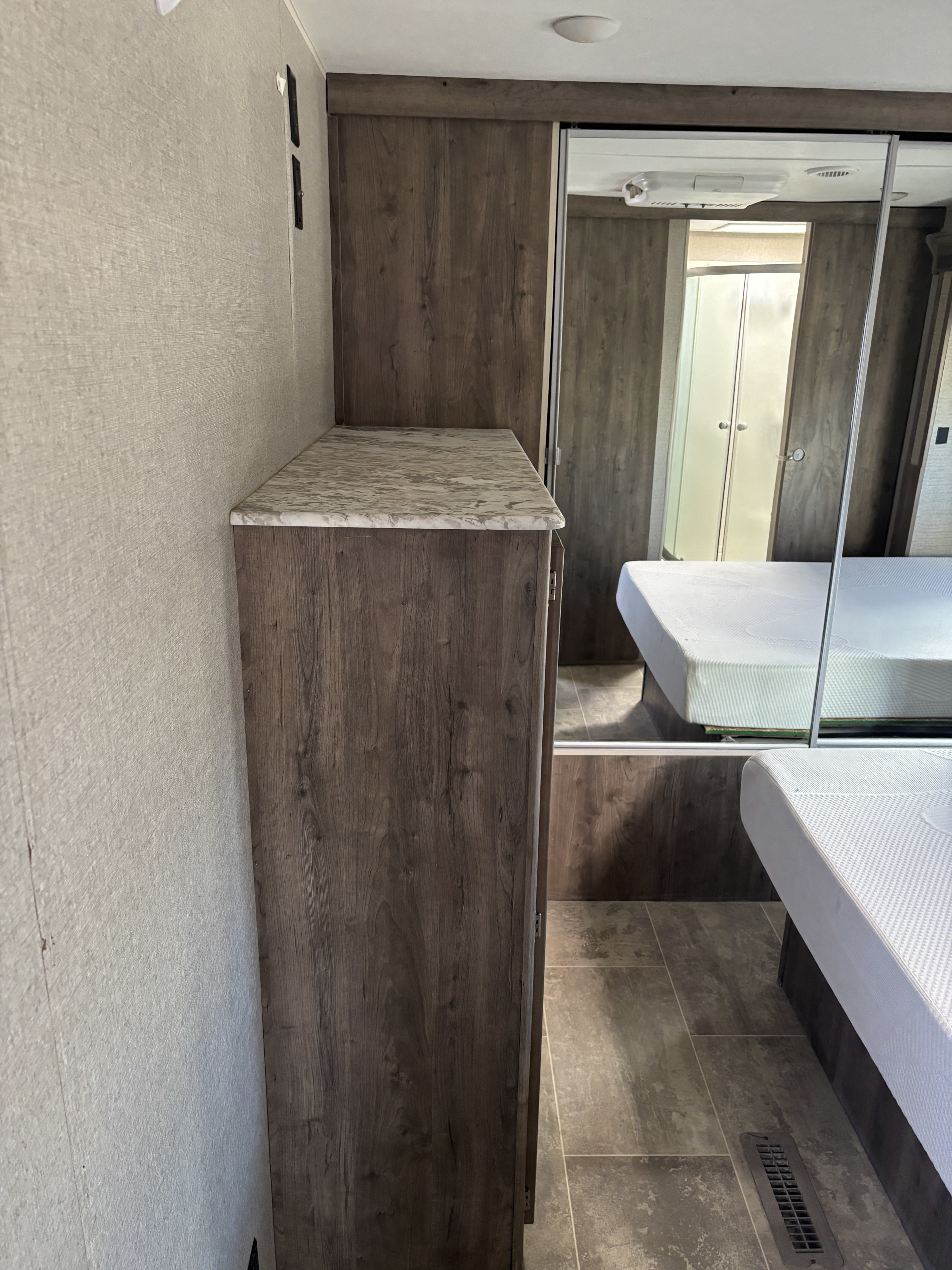 Inside this RV rental, a compact bedroom shows wood cabinetry, a mirrored closet, bed, and tiled floor.. Dutchmen Aspen Trail 2019