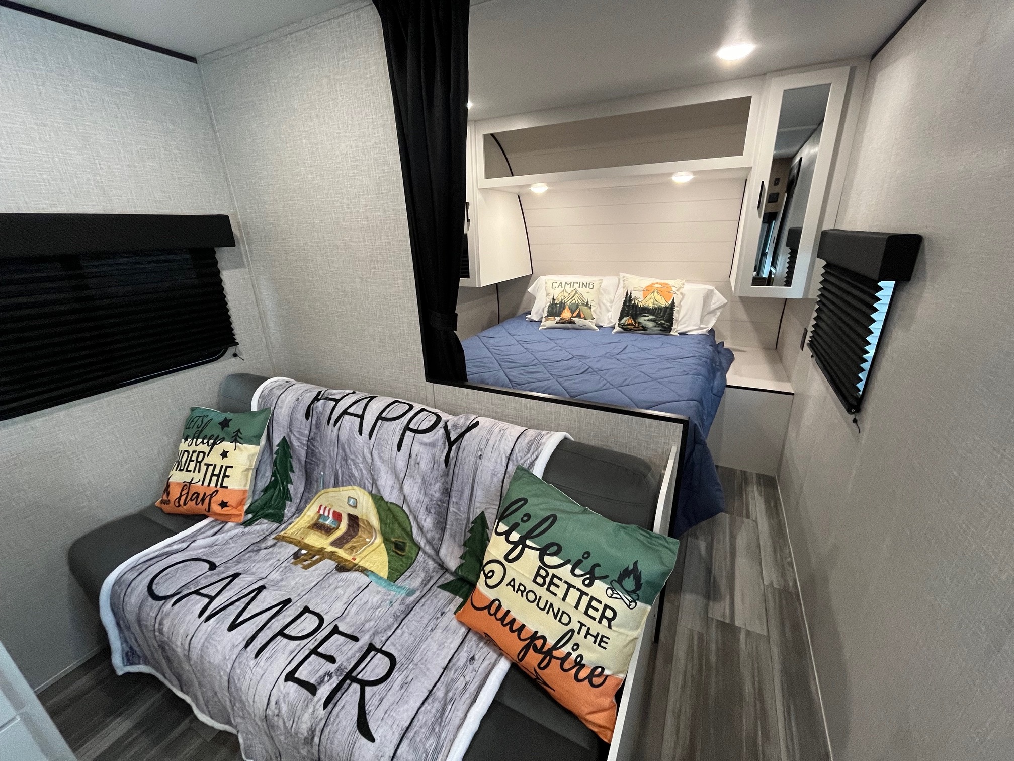 This inviting RV rental interior features a cozy bedroom with blue bedding and a living area with a "Happy Camper" blanket, perfect for travel.. Jayco Jay Flight SLX 2025