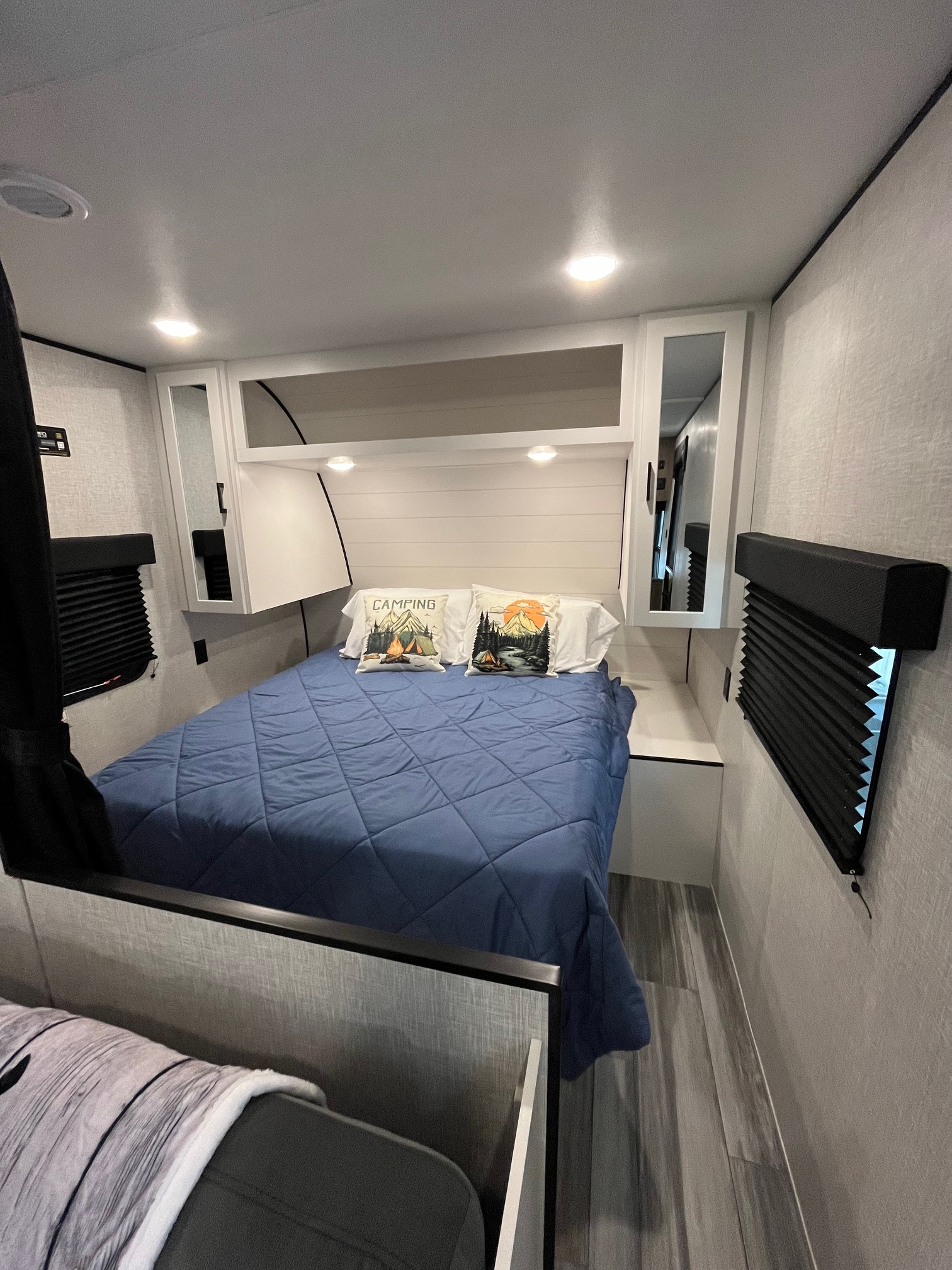 Inside a modern RV rental: a bright bedroom with a blue bed, camping pillows, overhead storage, and window blinds.. Jayco Jay Flight SLX 2025