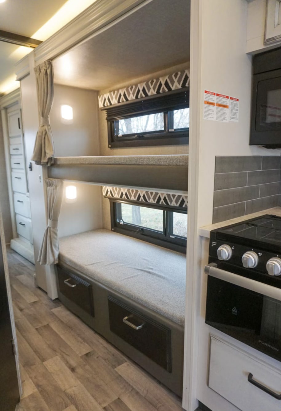 Cozy RV rental: Bunk beds with windows & personal lights, next to a compact kitchen with stove and oven.. Jayco Redhawk 2022