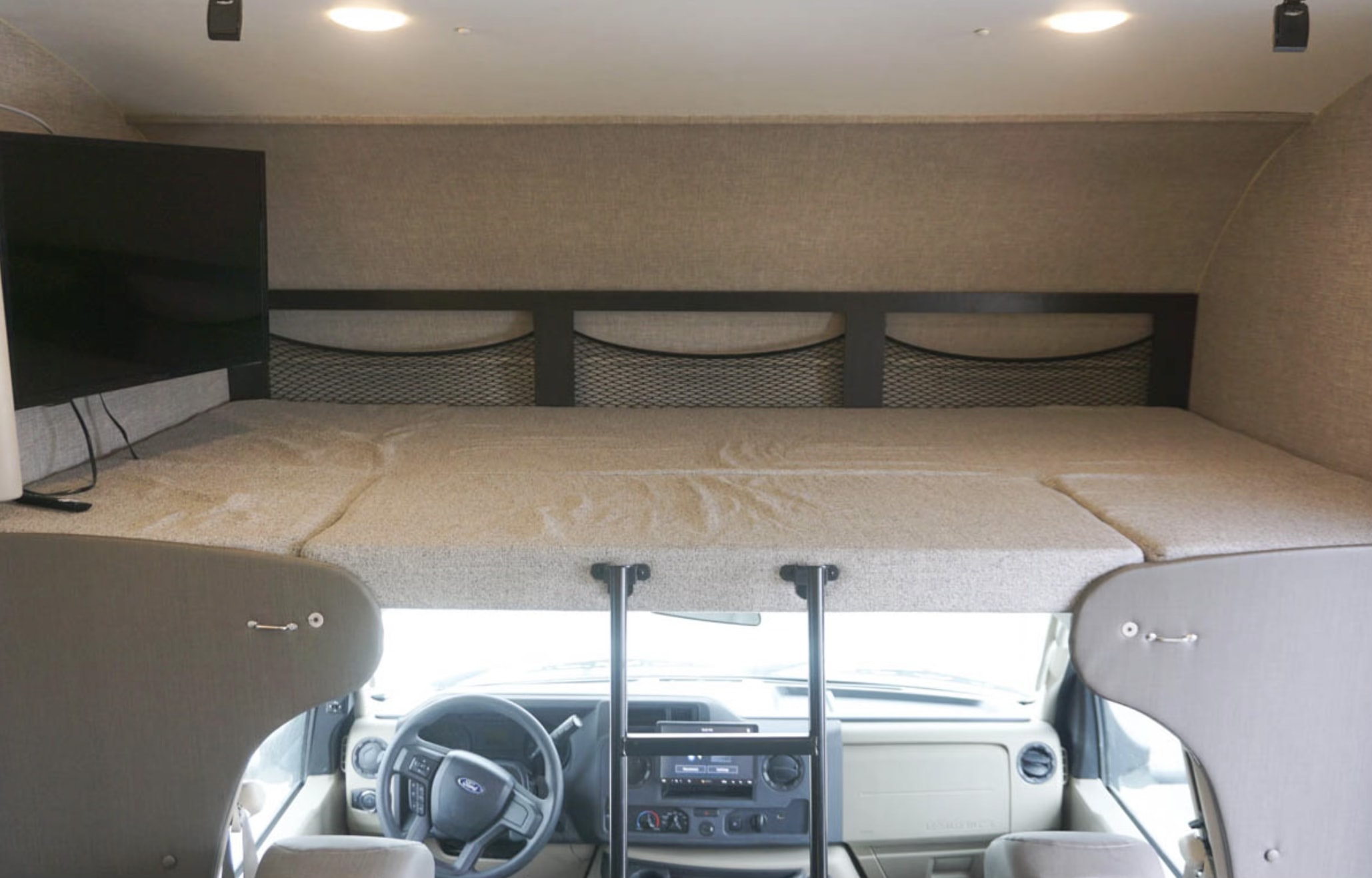Overhead bunk bed in an RV rental, complete with a TV, storage nets, and access ladder above the driving area.. Jayco Redhawk 2022