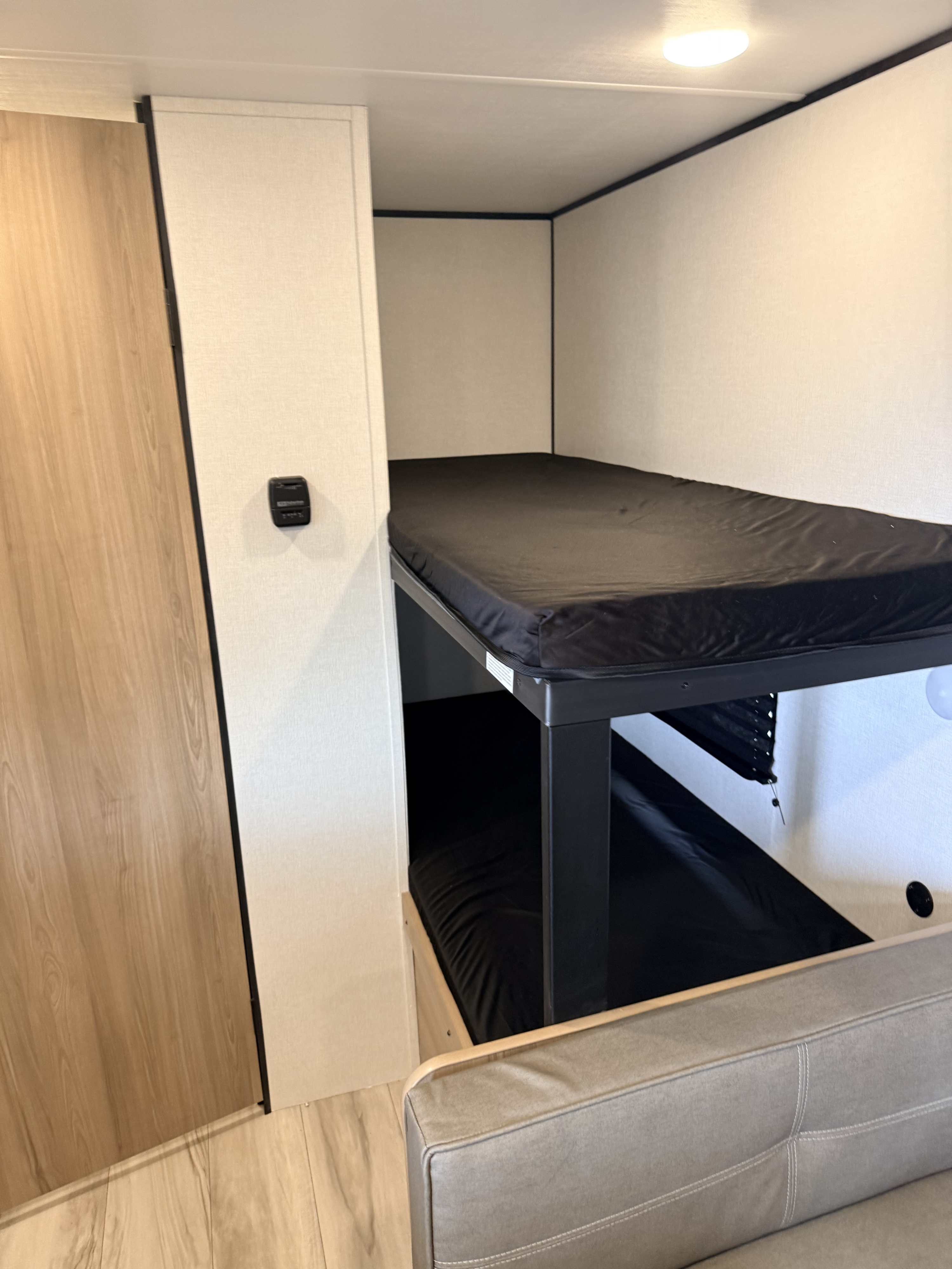 RV rental bunk beds with black mattresses, a wood door, and a cozy seating area, perfect for family trips.. Keystone Coleman 17B 2026