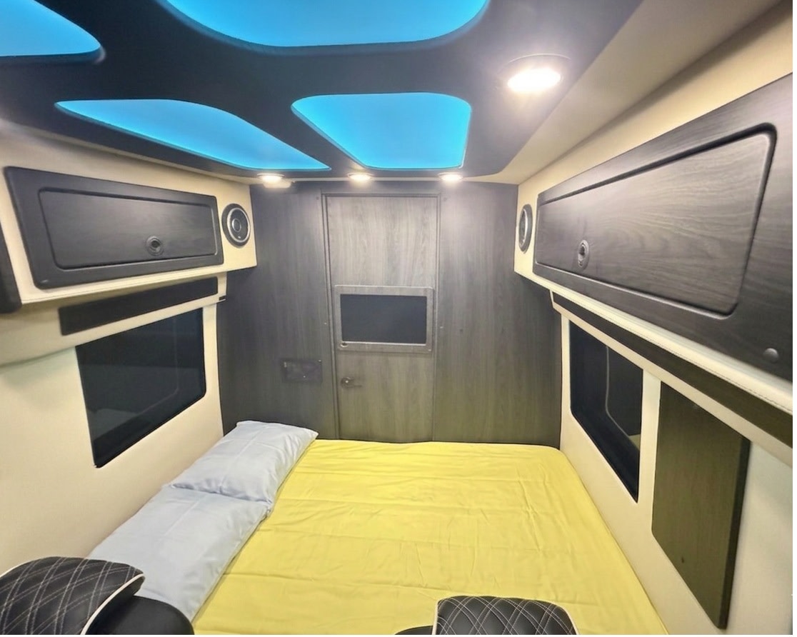 Modern RV rental bedroom: Features a comfortable yellow bed, sleek storage, and blue ambient lighting. Ideal for mobile adventures.. OGV Luxury Coach V-Cruise 2026