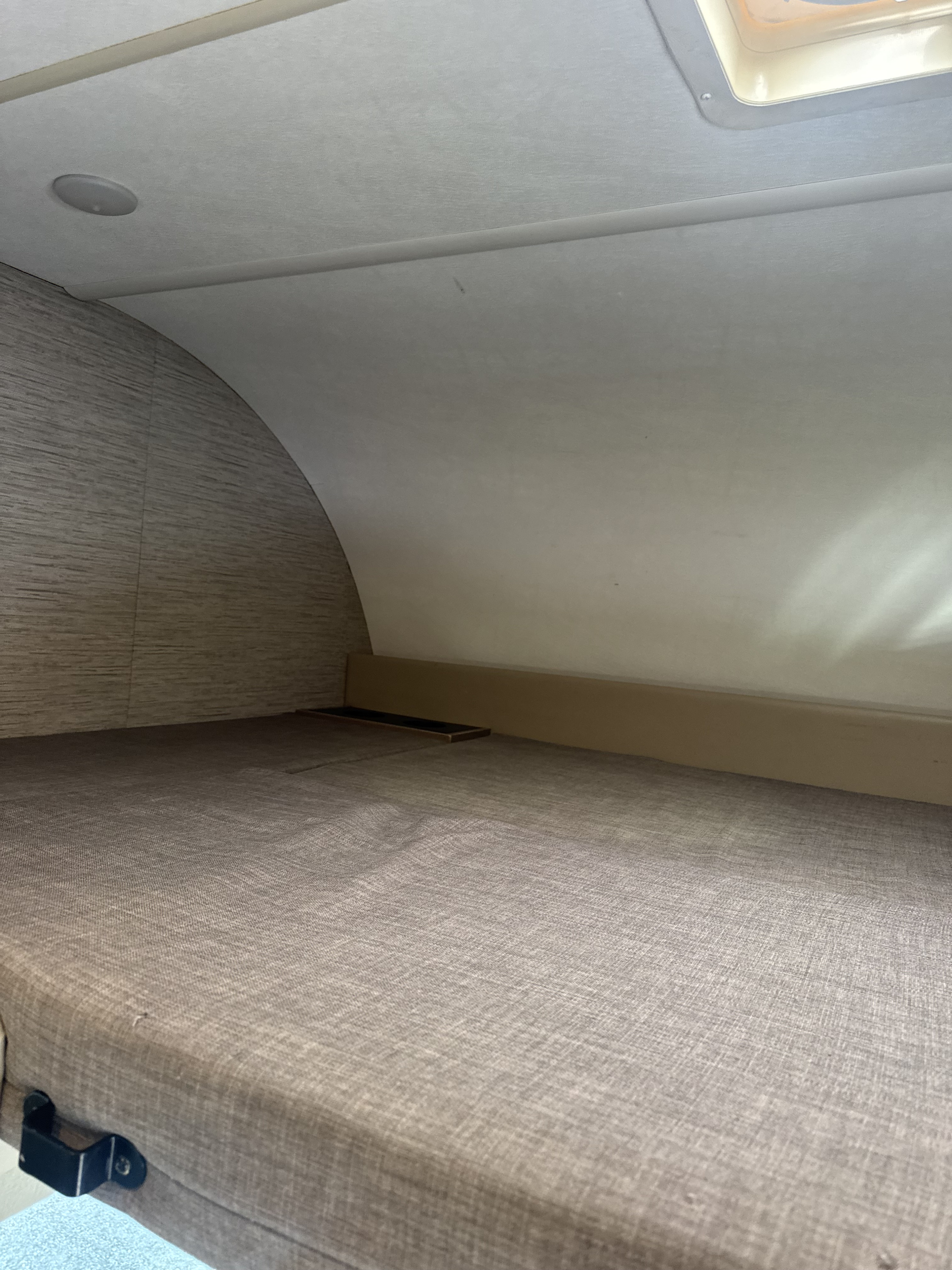 Inside an RV rental: a cozy bunk bed with curved, textured walls, ceiling light, and skylight above. Ready for rest.. Thor Four Winds 2022