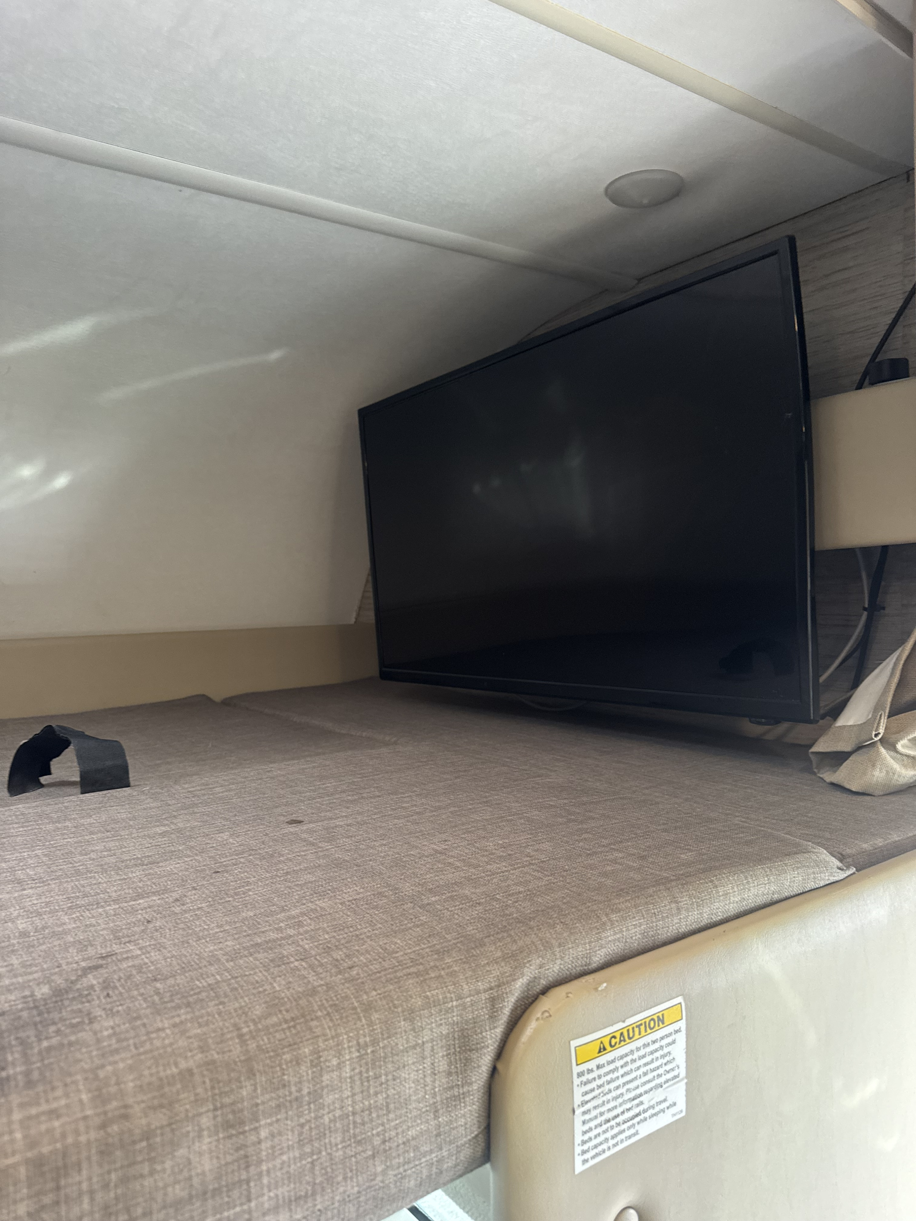 RV rental: Elevated bunk bed with a TV and a 'CAUTION' sticker about the 800 lbs max load for the two-person bed.. Thor Four Winds 2022