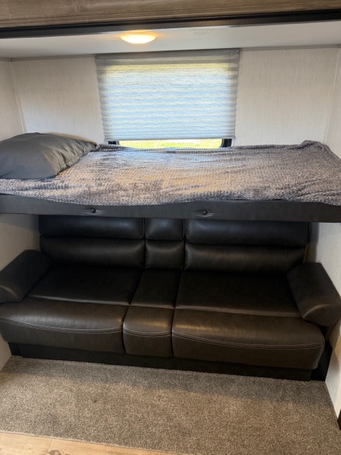 This RV rental interior shows a bunk bed with a grey blanket above a black sofa. Perfect for a cozy night's sleep or relaxation.. Forest River Cherokee Grey Wolf 2022