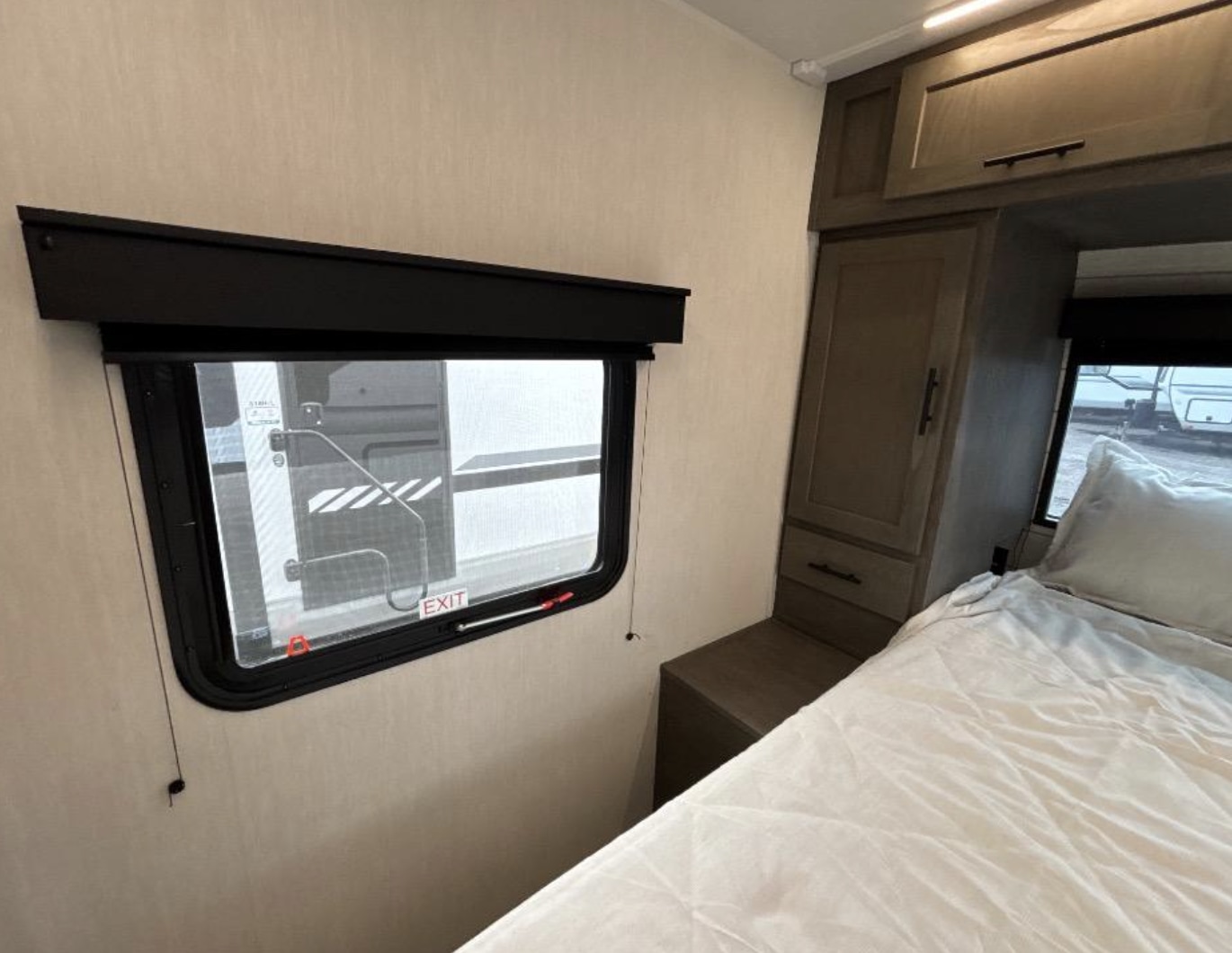 Cozy RV rental bedroom with a window showing an outside view, a comfortable bed, and built-in cabinets for storage.. Forest River Alpha Wolf 2025
