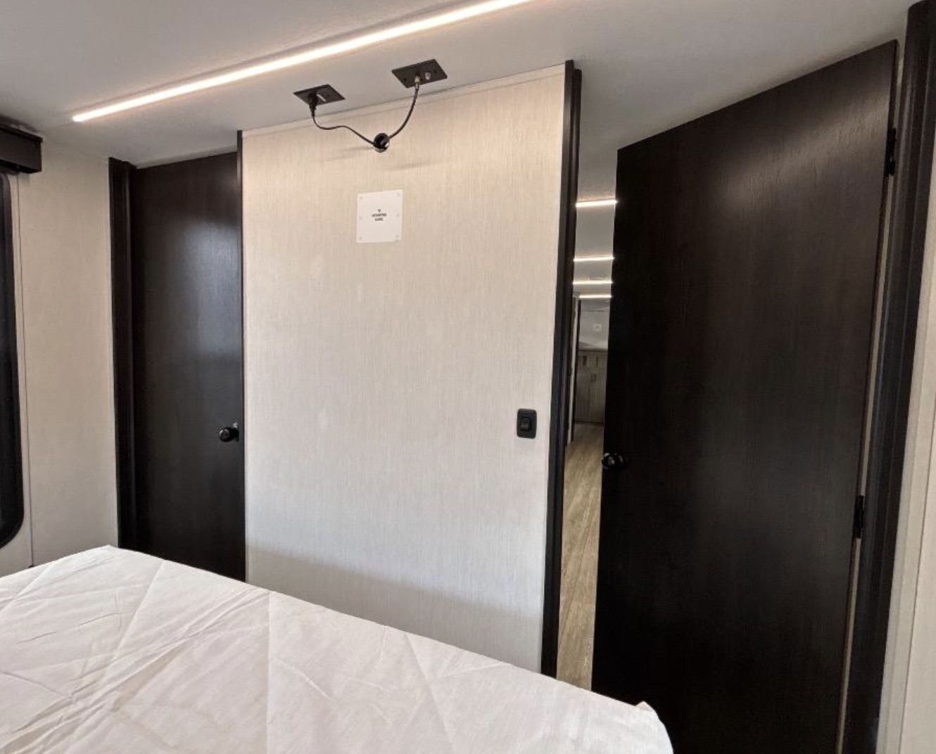 RV rental bedroom view: a divider wall with TV mount, dark doors on each side, and modern ceiling lights.. Forest River Alpha Wolf 2025