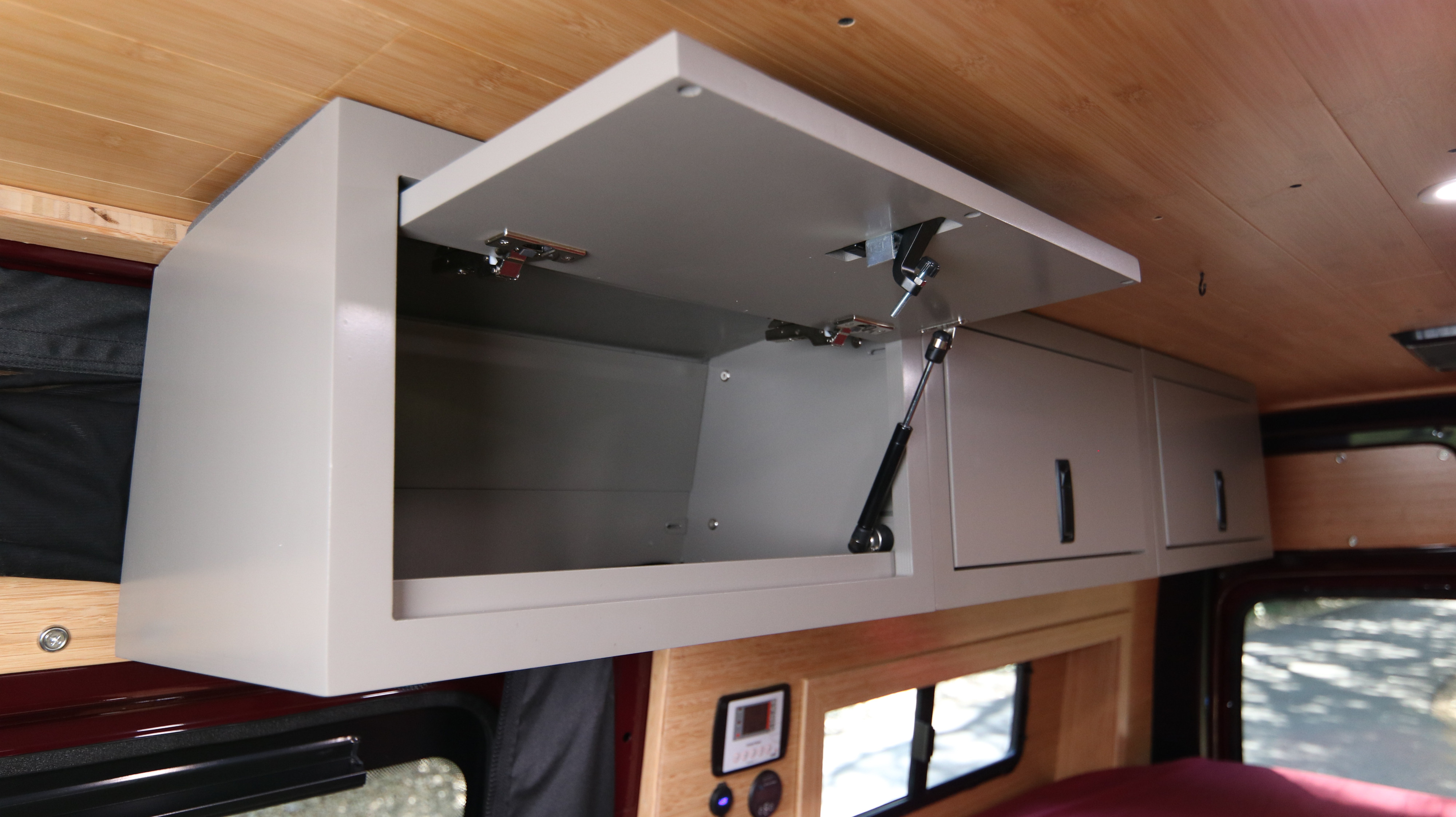 RV rental camper van: open light-gray overhead storage cabinet, wooden ceiling, and a control panel visible.. Mercedes-Benz Sprinter 2025