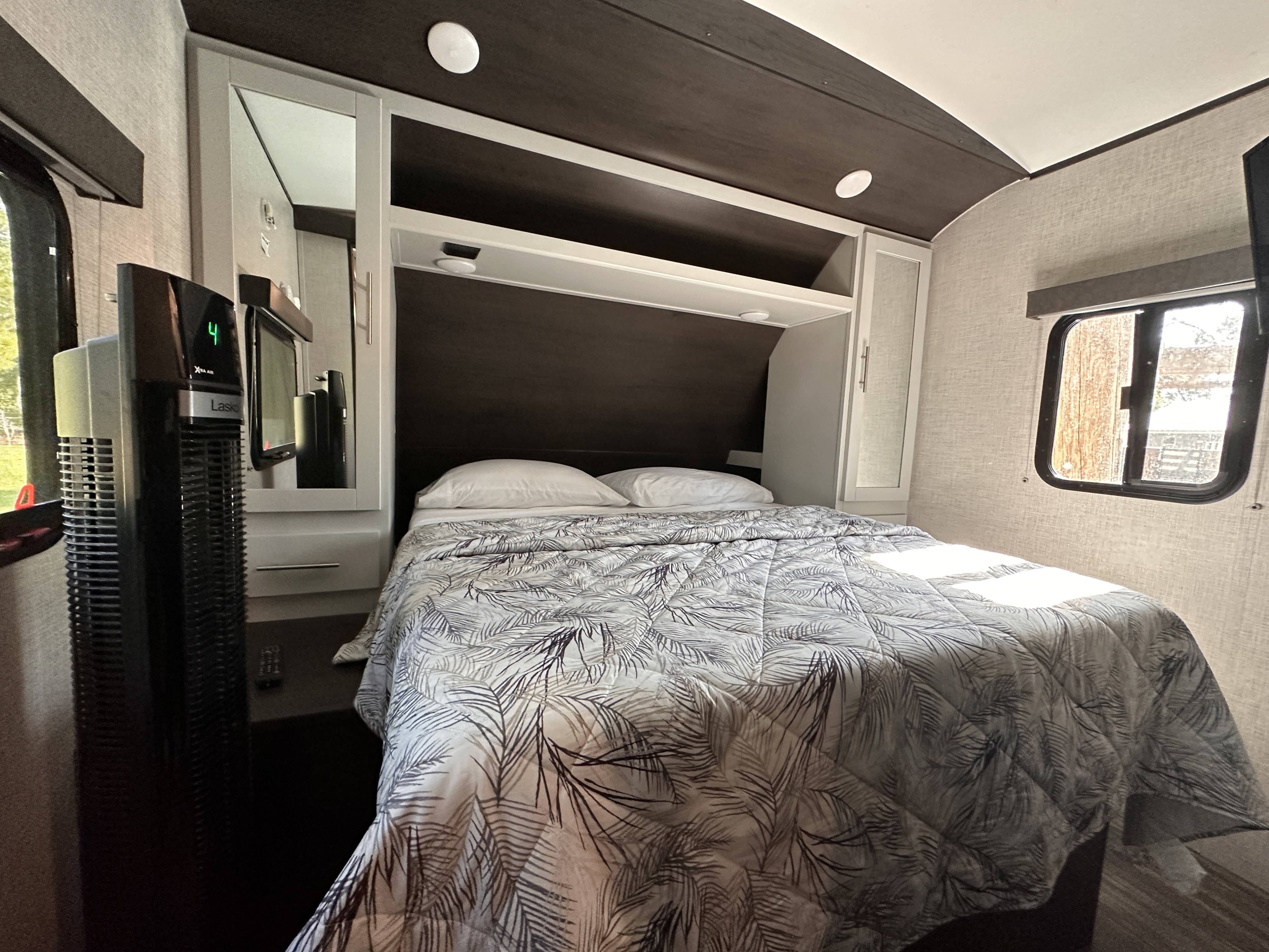 Inside an RV rental bedroom: a bed with a white and gray palm-leaf comforter, pillows, shelving, and a tall fan.. Keystone RV Bullet Ultra Lite 2020