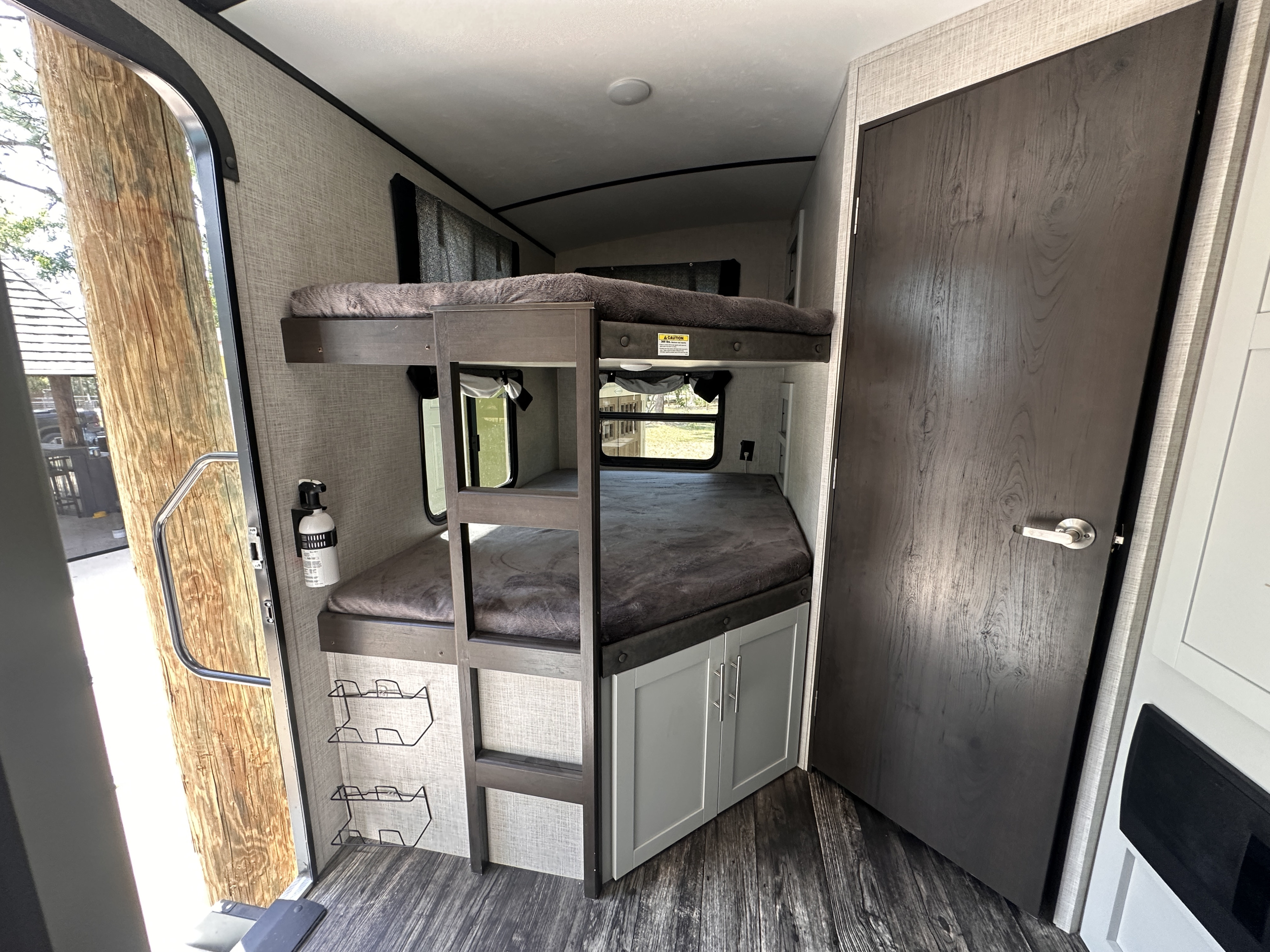 RV rental interior featuring cozy bunk beds, a fire extinguisher, storage cabinets, and a door open to nature.. Keystone RV Bullet Ultra Lite 2020