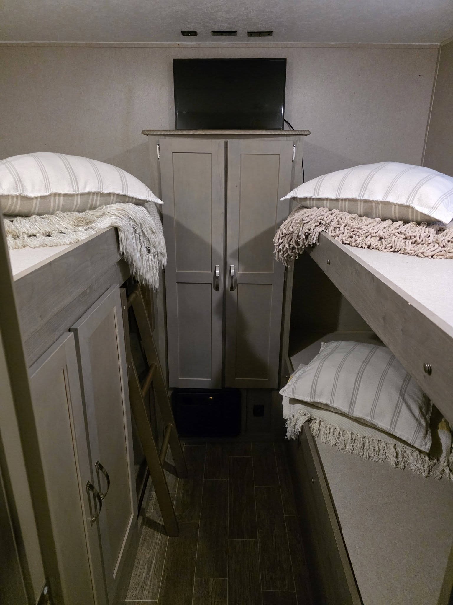 RV rental interior: Two bunk beds with pillows and throws, a central cabinet with TV, and a ladder in a compact sleeping area.. Palomino puma 2020