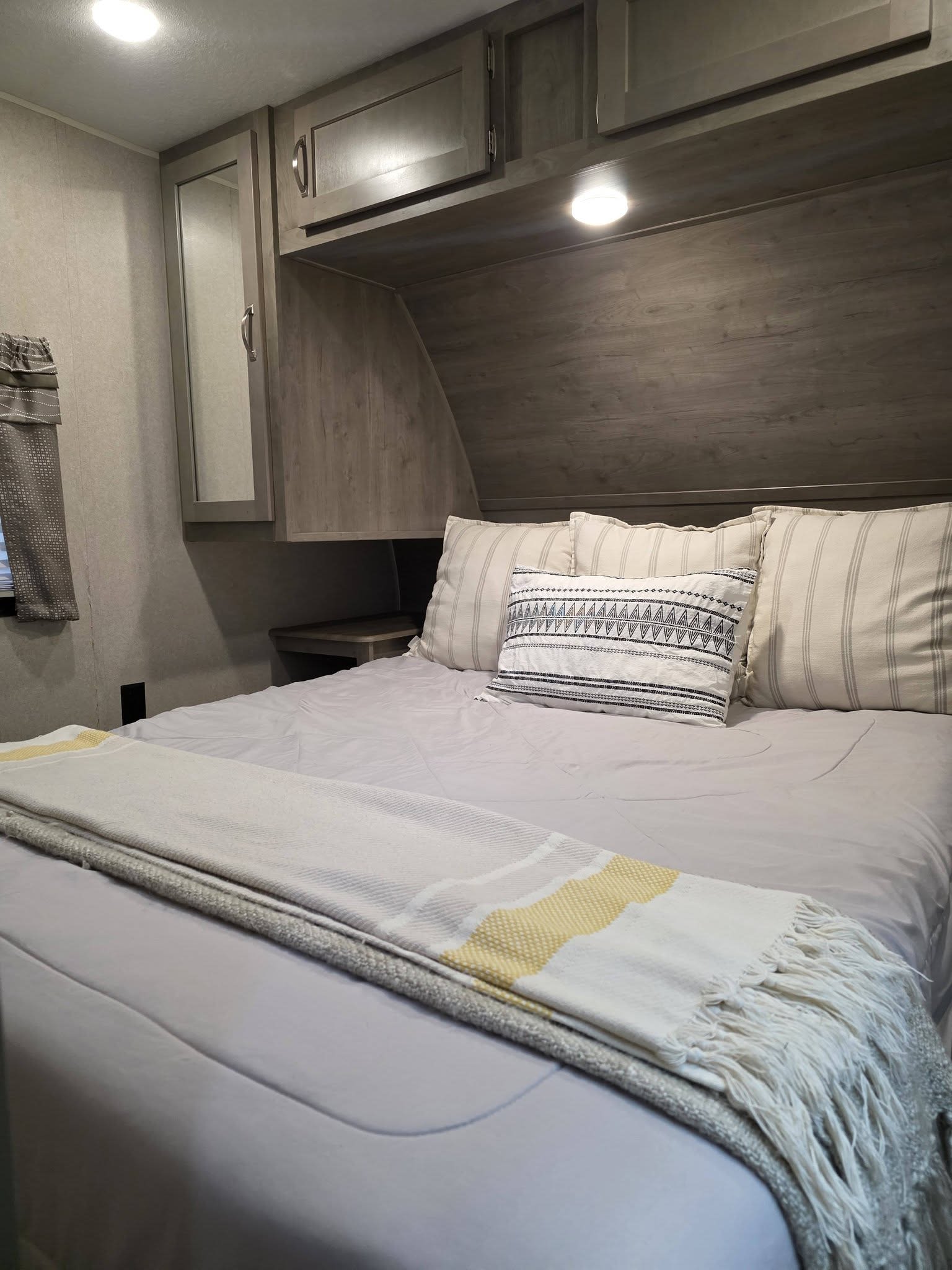 Serene RV rental bedroom: light gray bedding, striped pillows, and wooden overhead cabinets for a cozy stay.. Palomino puma 2020