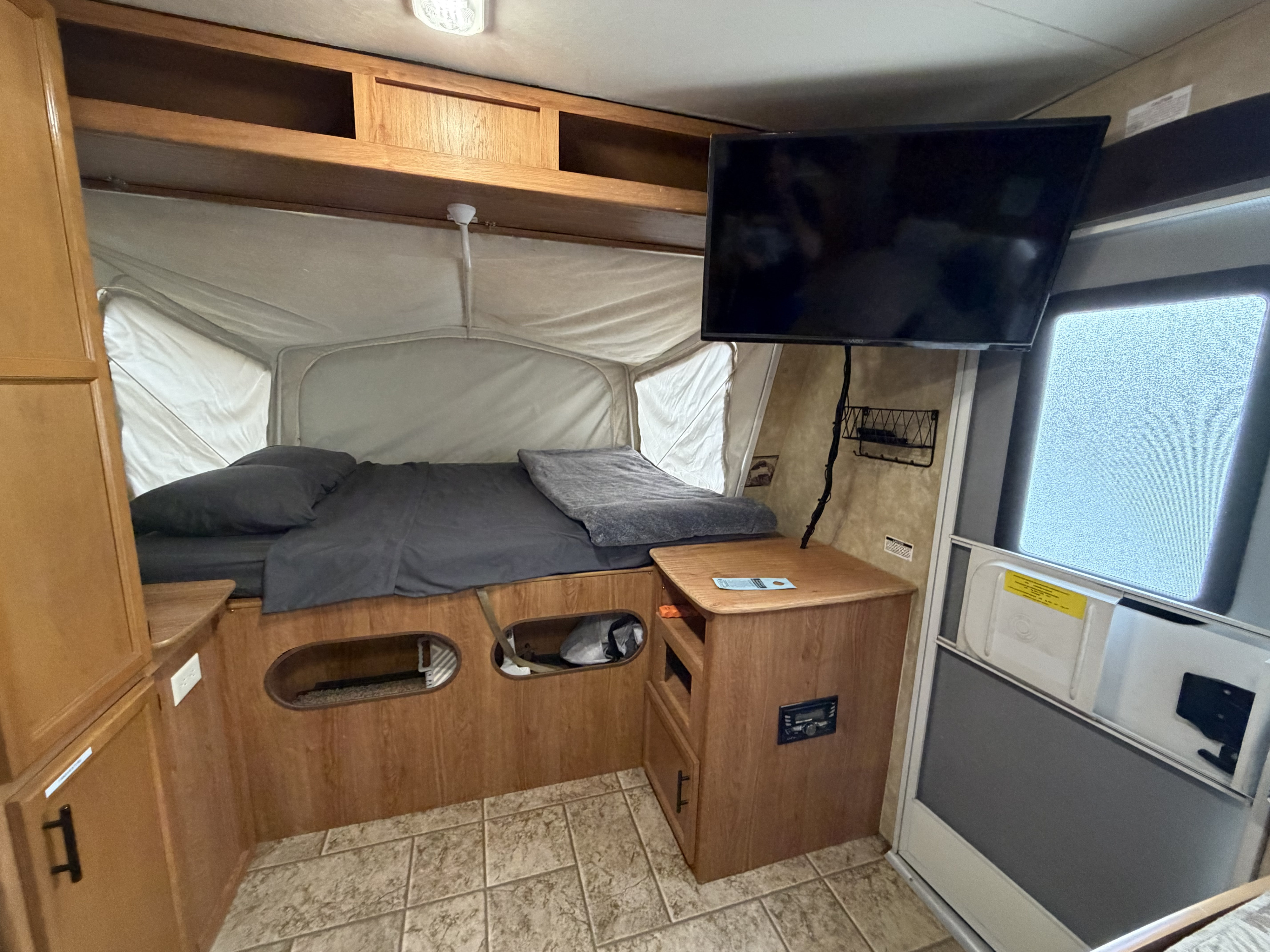 RV rental: Interior of a pop-up camper with a bed, mounted TV, wooden storage, and tiled floor.. Jayco Jay Feather EXP 2010