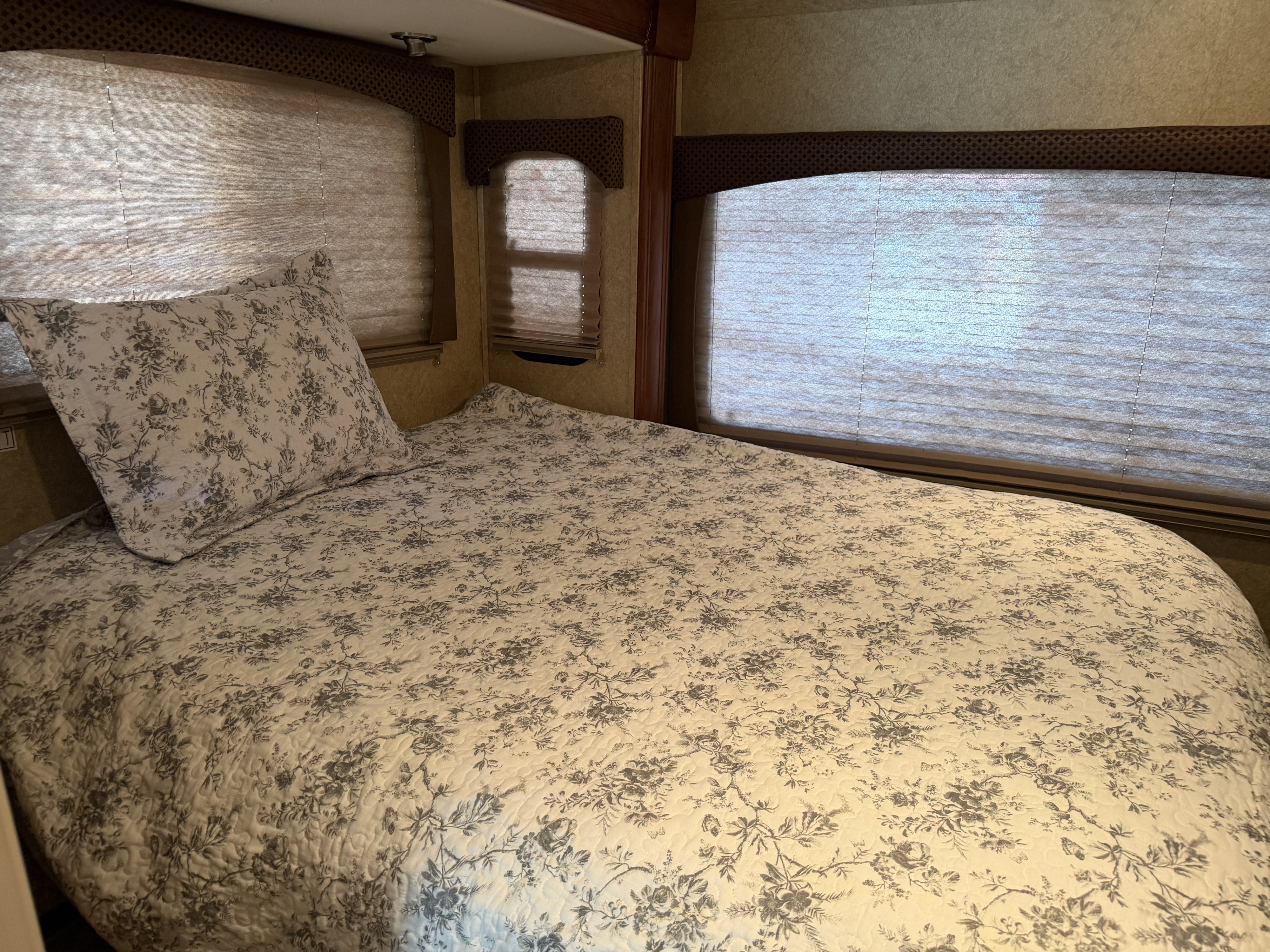 Cozy RV rental bedroom featuring a bed with a white and gray floral quilt, pillow, and multiple pleated window blinds.. Forest River Forester 2013