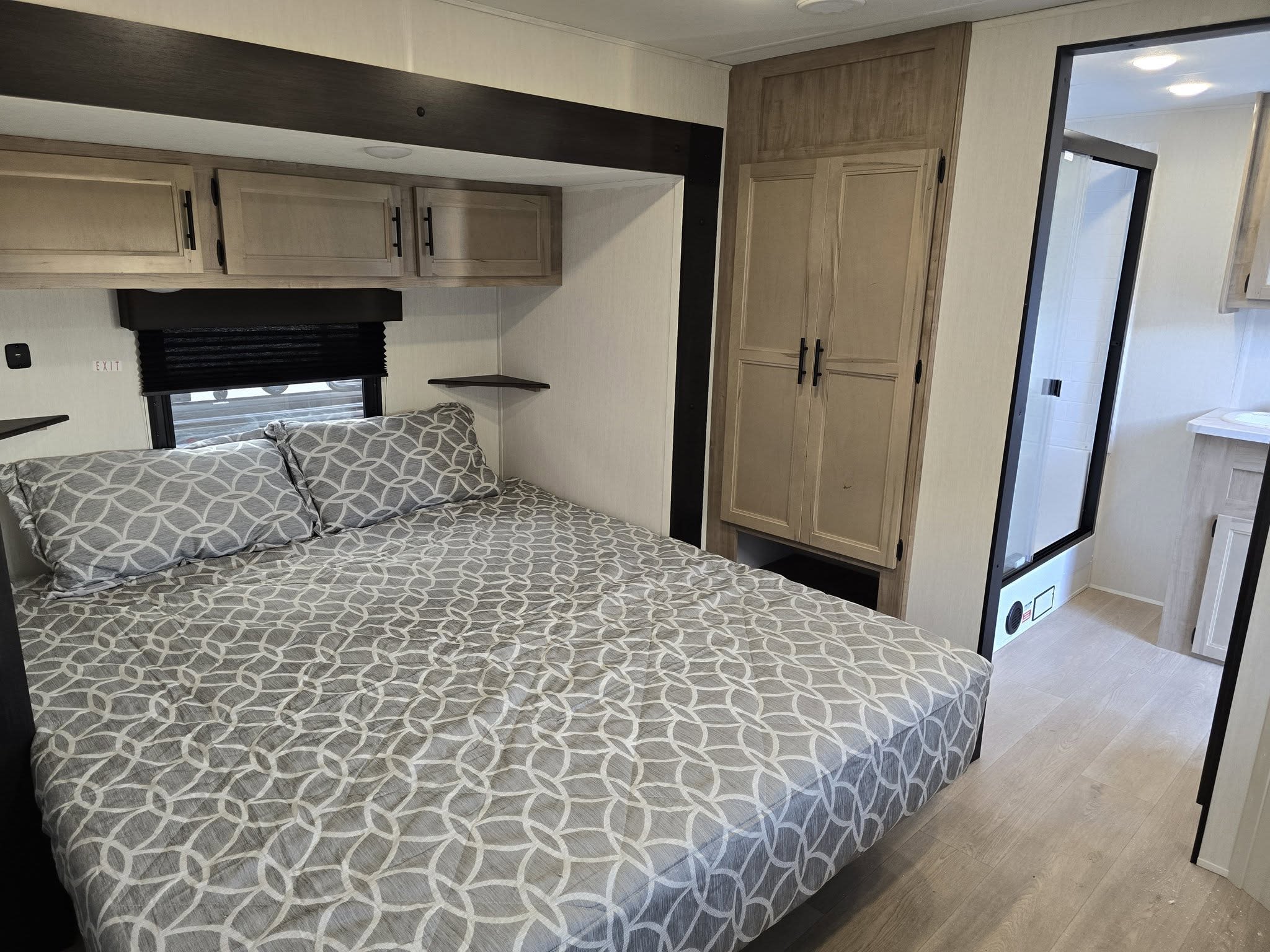 RV rental bedroom with a comfortable bed, overhead cabinets, wardrobe, and an attached bathroom with a visible shower.. Forest River Cherokee Timberwolf 2025