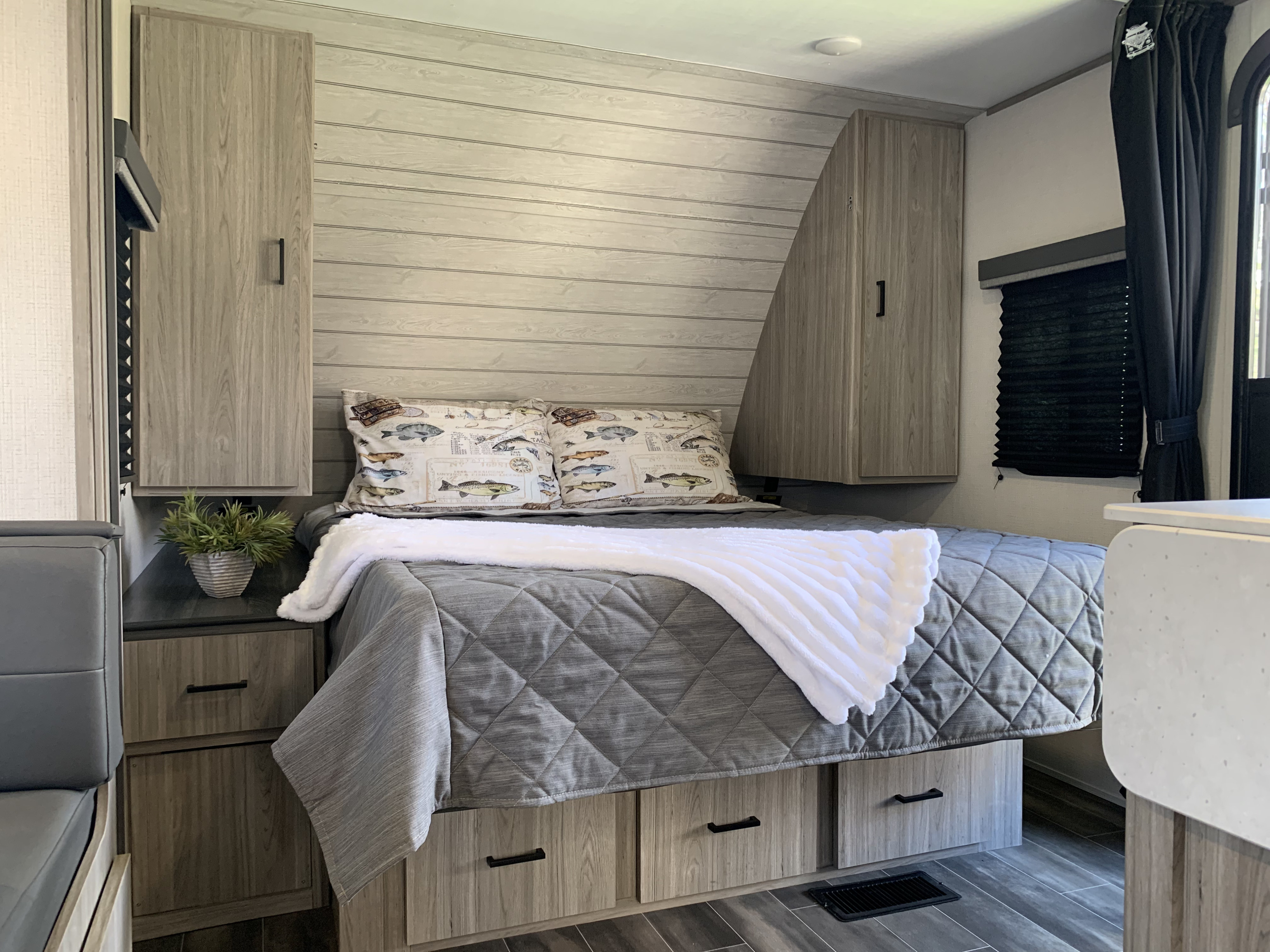 Cozy rv rental bedroom: bed with fish pillows, wood-paneled walls, overhead cabinets, and under-bed storage.. Keystone RV Passport 2022
