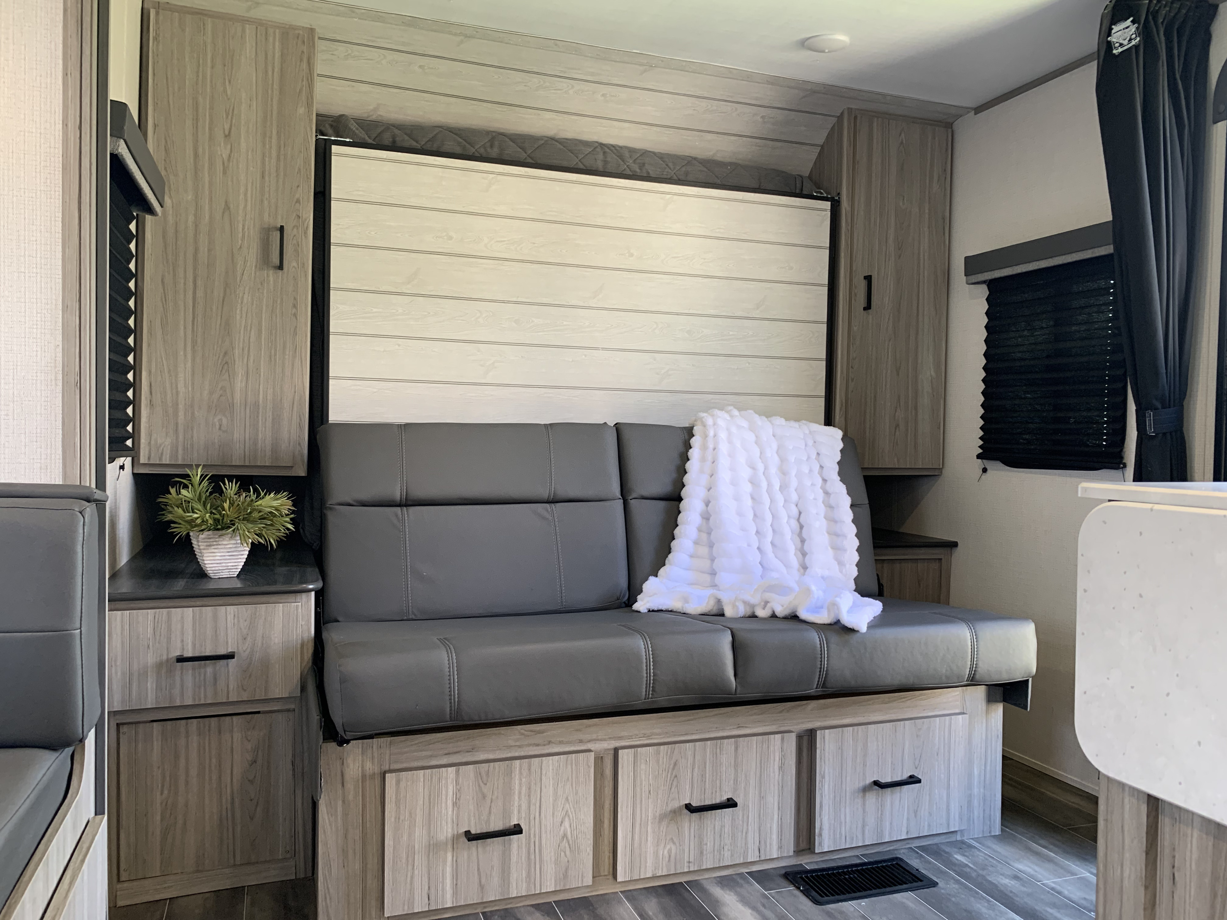 Cozy RV rental interior with a gray sofa, folded murphy bed, wooden storage, and a soft white blanket.. Keystone RV Passport 2022