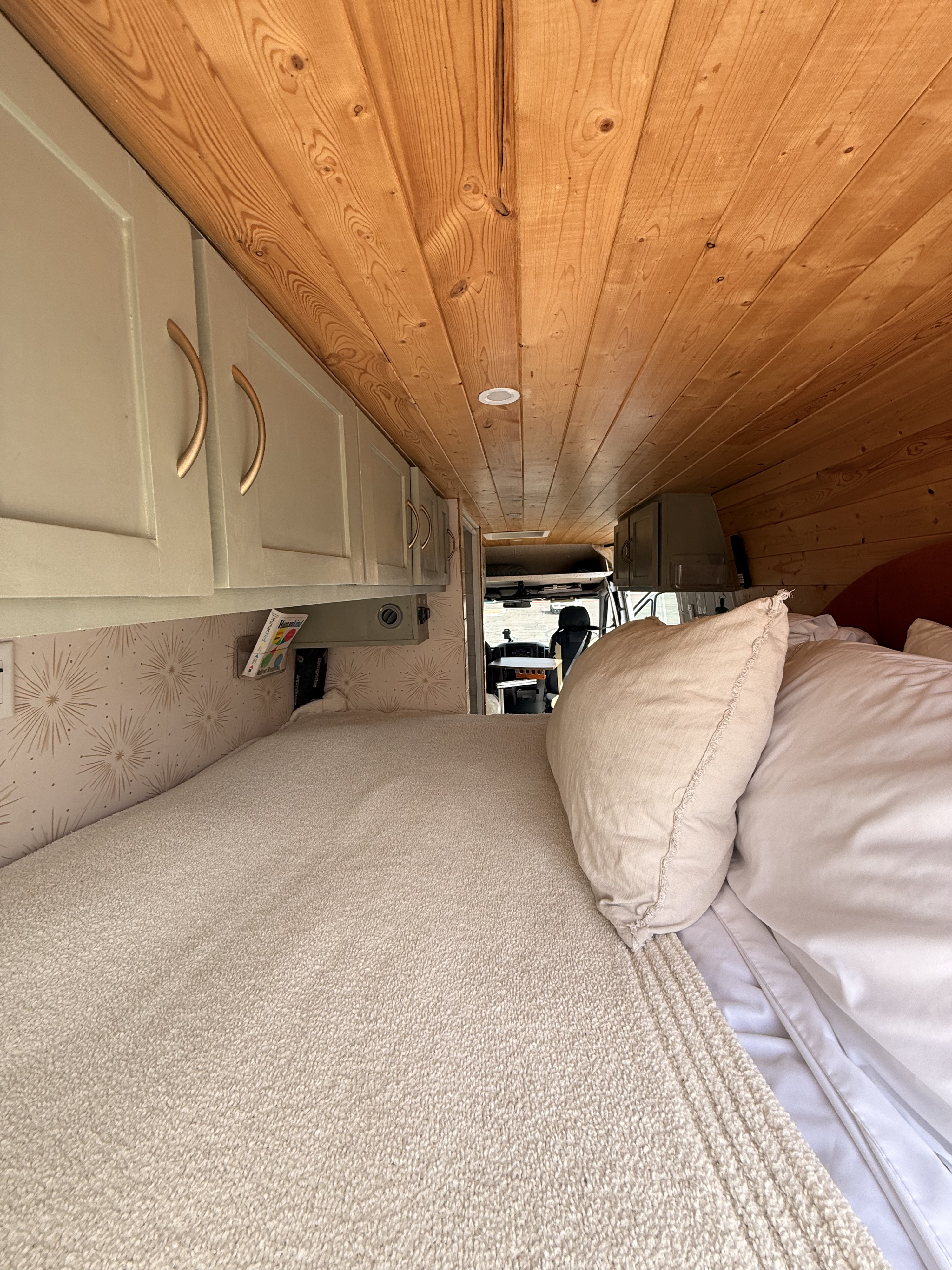 Cozy RV rental interior featuring a wood-paneled ceiling, light gray cabinets, and a comfortable bed with pillows.. Mercedes-Benz Sprinter 2011