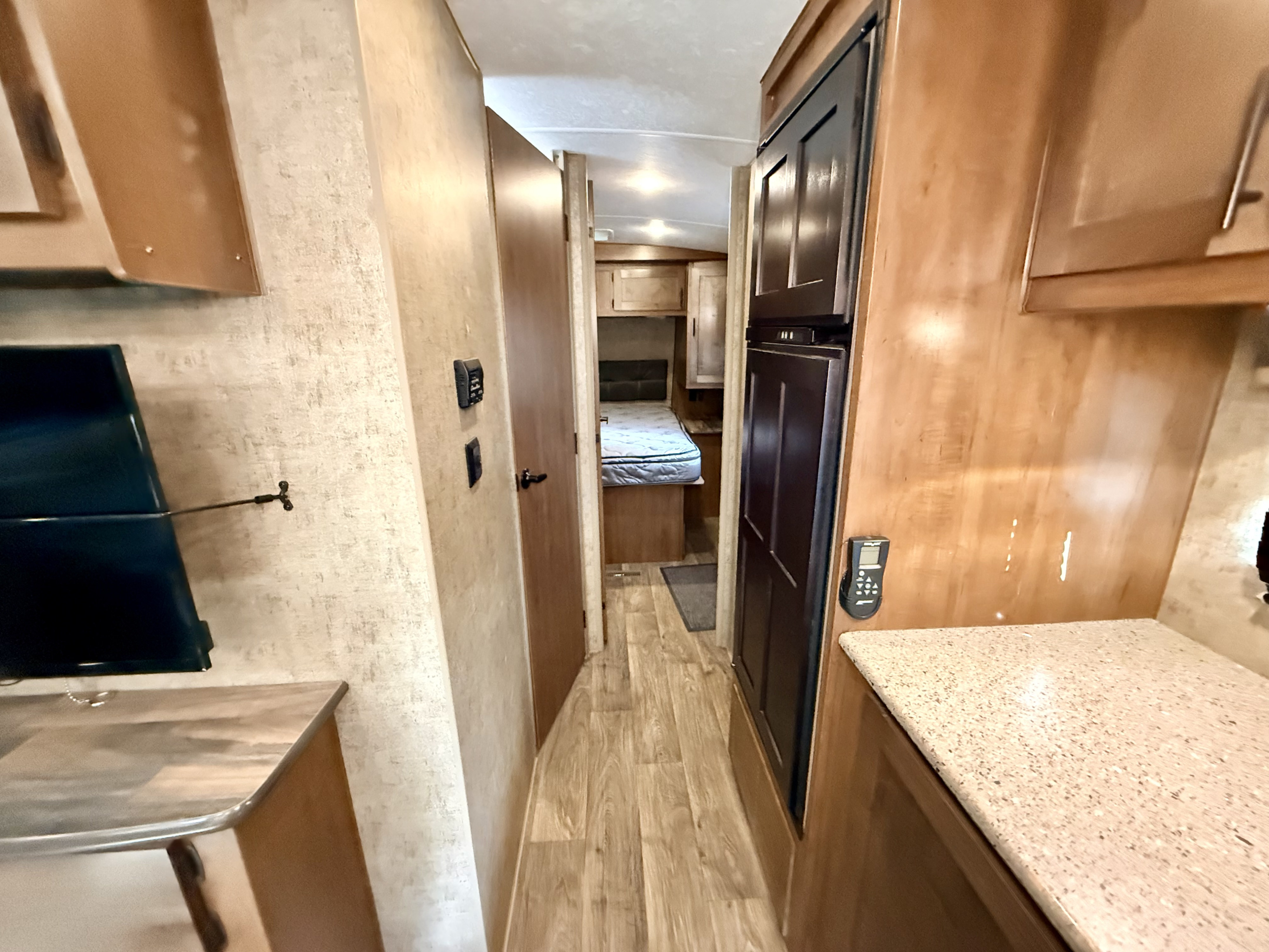 RV rental interior: a central hallway leads to the bedroom, with a full-sized fridge, countertop, and TV mount visible.. Outdoors RV Mountain 2021