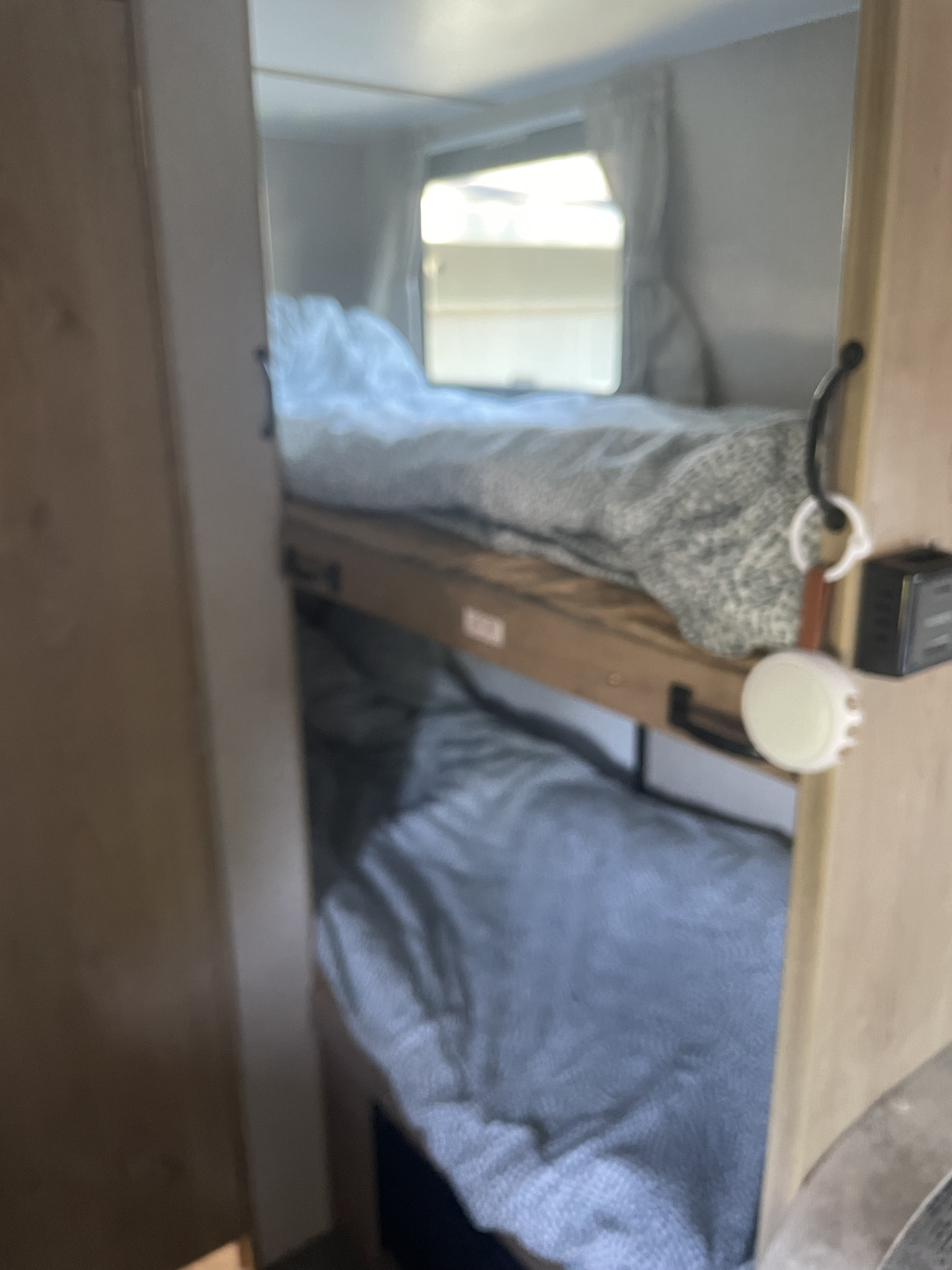 Cozy bunk beds in this rv rental, neatly made with blankets. A bright window is visible above the top bunk; a hook hangs on the right.. Winnebago Micro Minnie 1700BH 2019