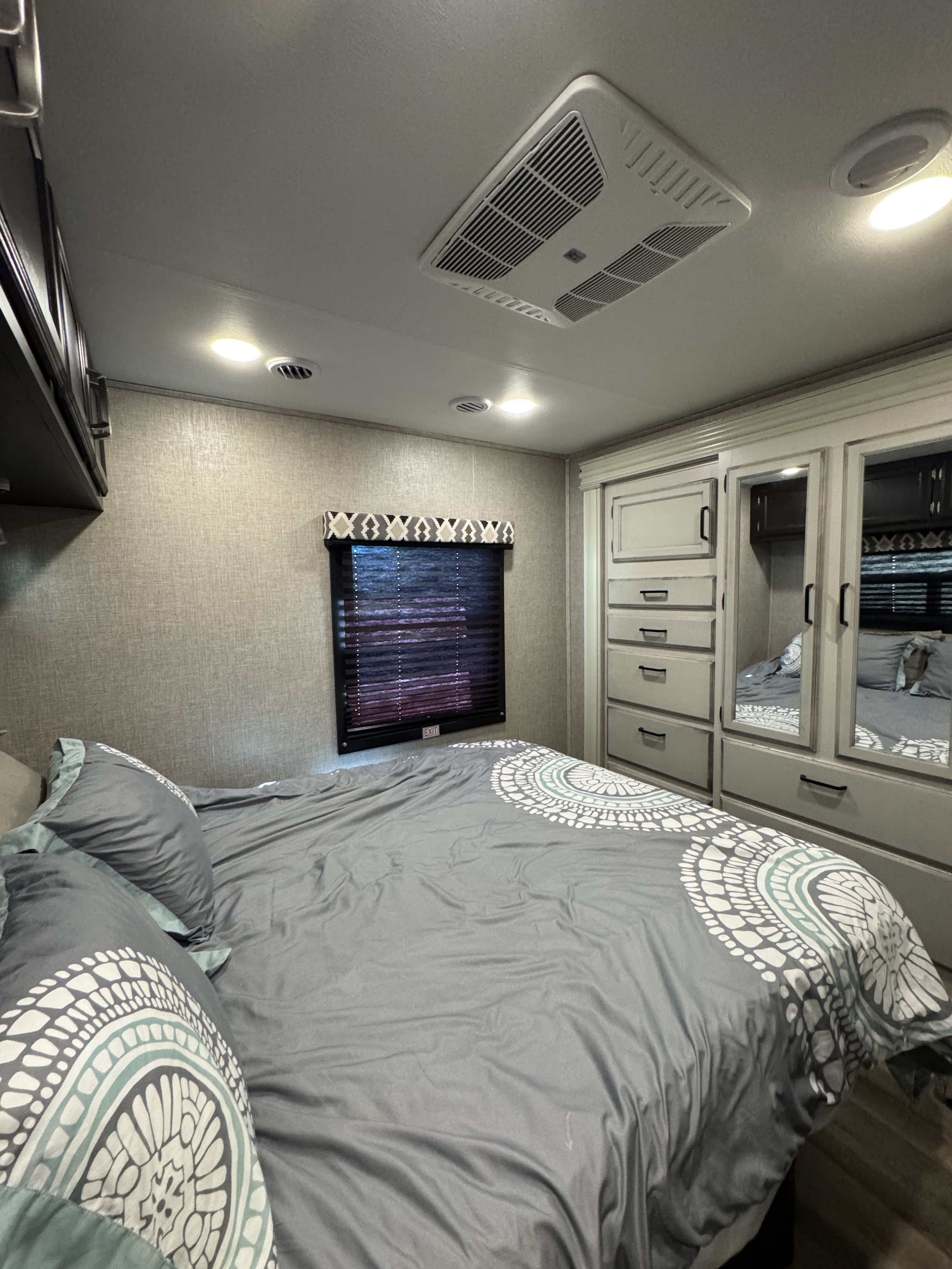 Cozy RV rental bedroom with gray patterned bedding, built-in storage, window, and AC unit overhead.. Jayco Redhawk 2022