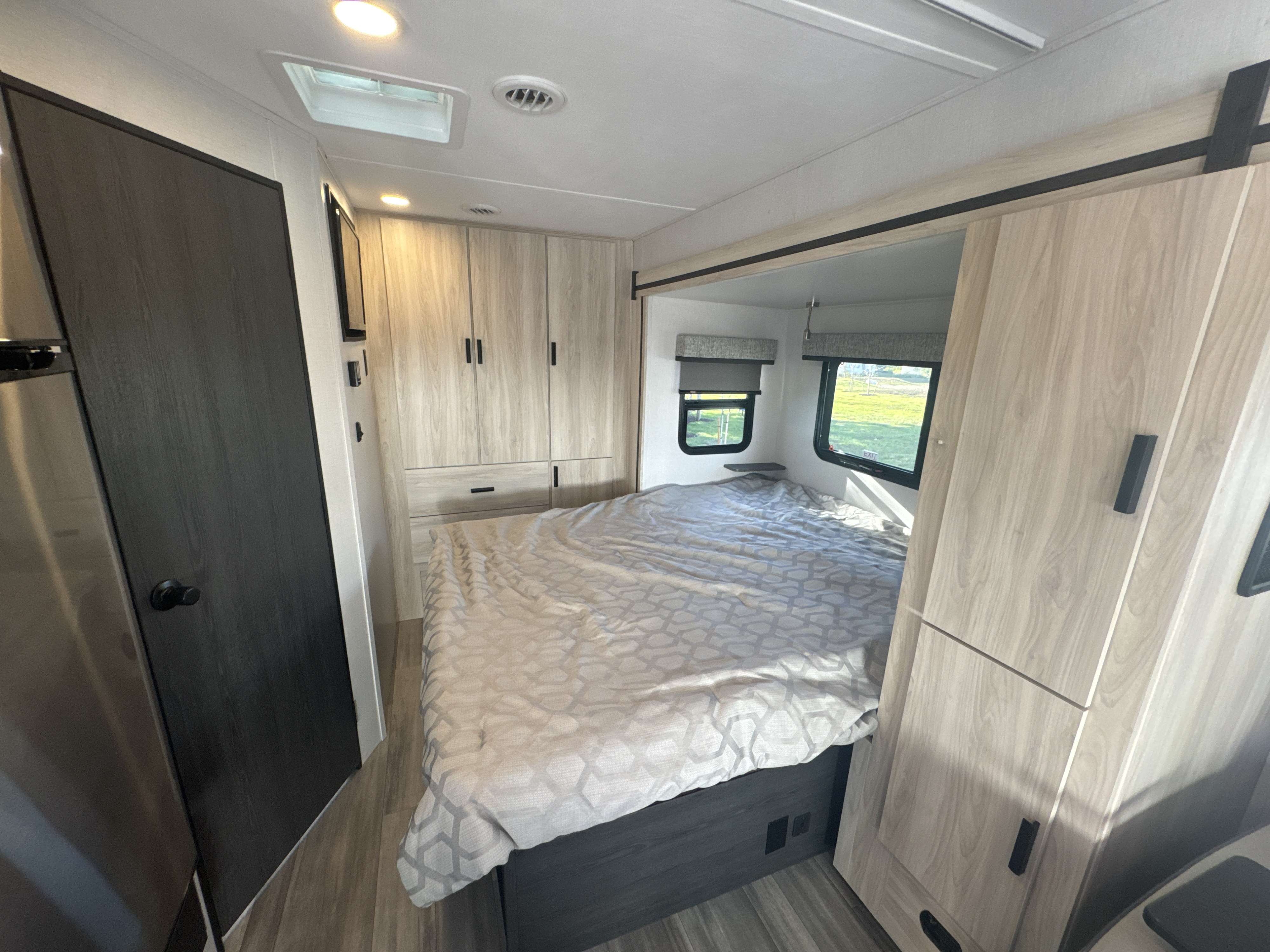 Inside an RV rental, this bright bedroom features a comfortable bed, light wood cabinets, and two windows with blinds.. Forest River Sunseeker MBS 2023