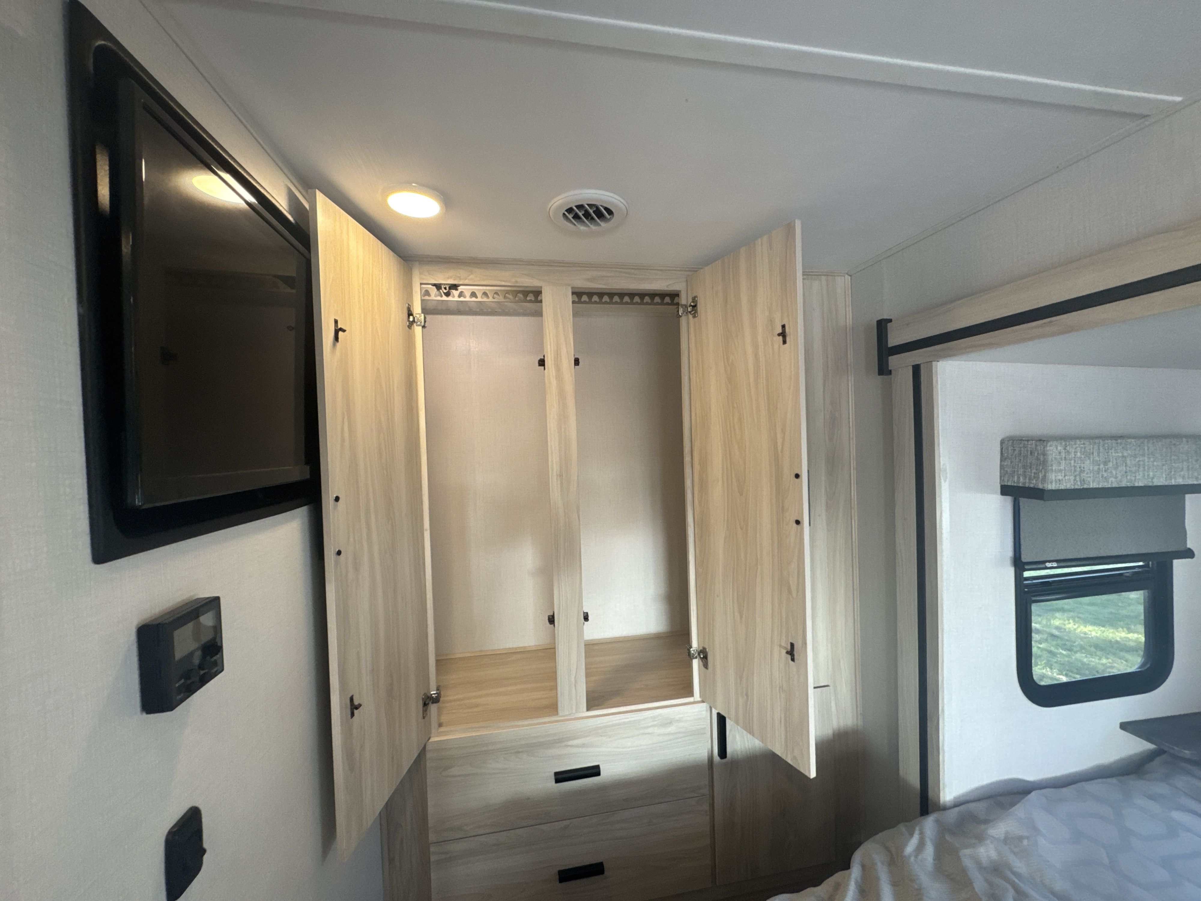 RV rental bedroom: an open closet with hanging rods & drawers. Also seen: TV, AC vent, ceiling light, & bed.. Forest River Sunseeker MBS 2023
