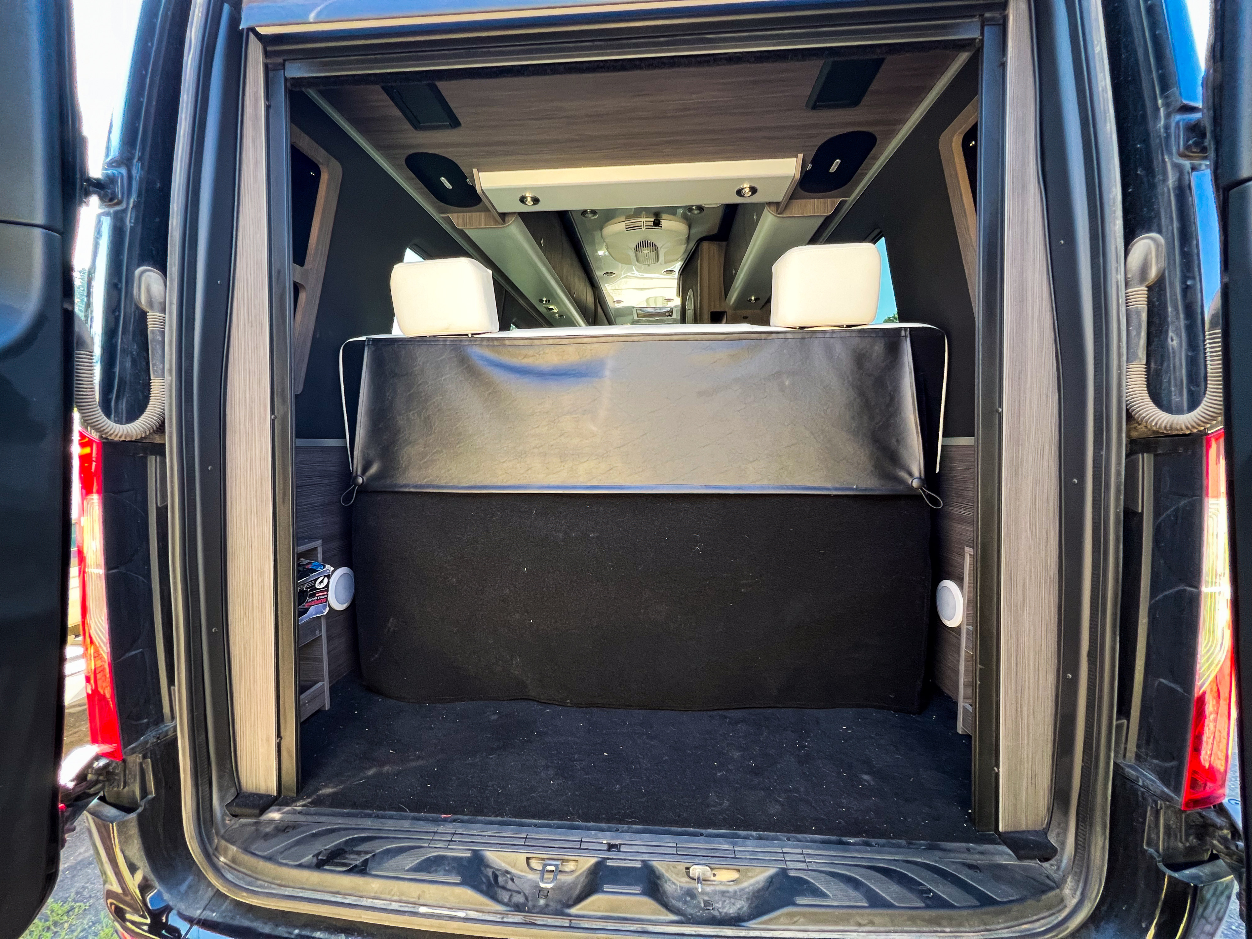 RV rental camper van interior: Rear view showing black upholstered bench, white headrests, wood panels, and overhead lighting.. Airstream Interstate 2022
