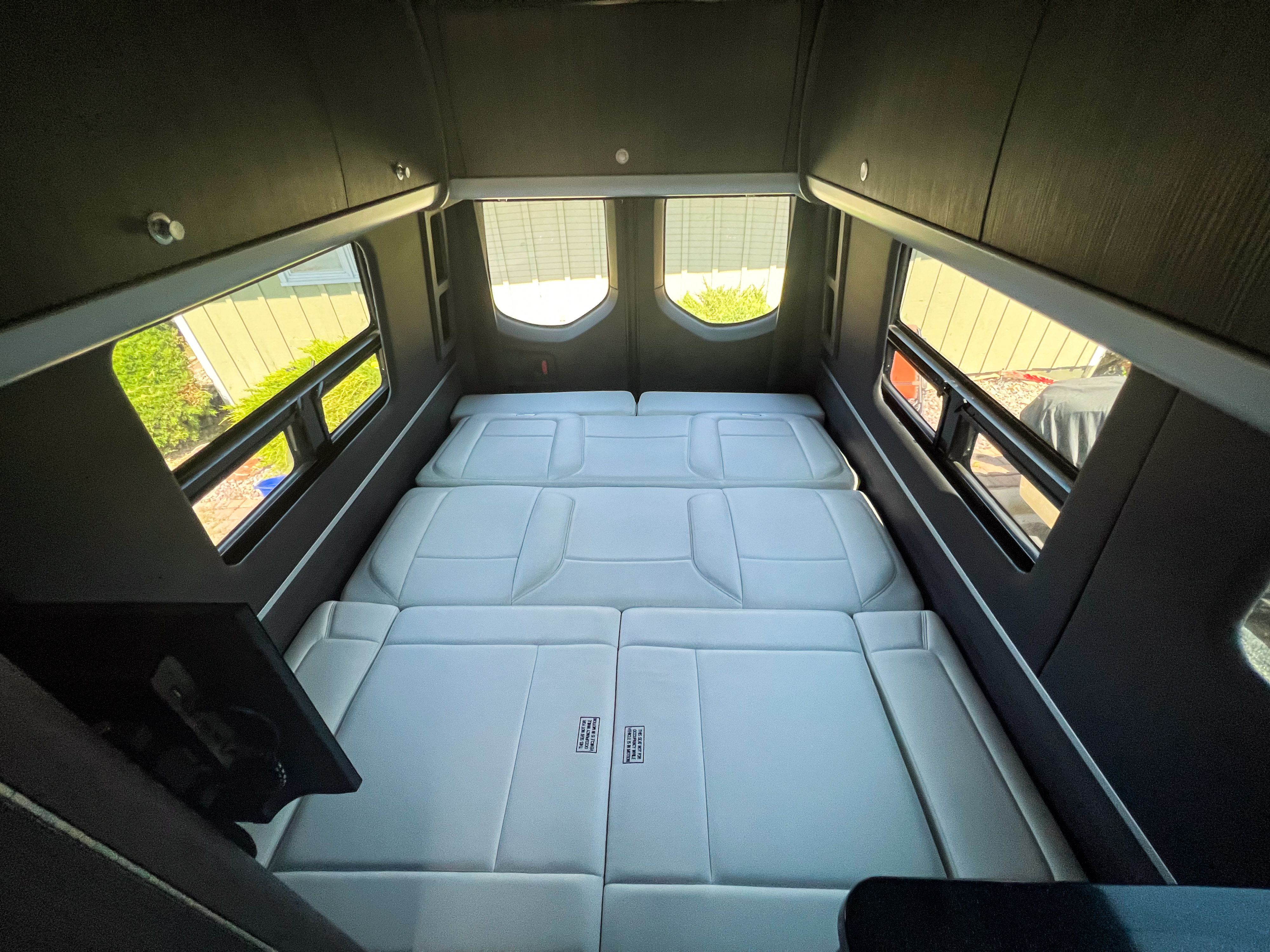 RV rental: View of a modern camper van's rear interior with a gray modular bed setup and bright windows.. Airstream Interstate 2022