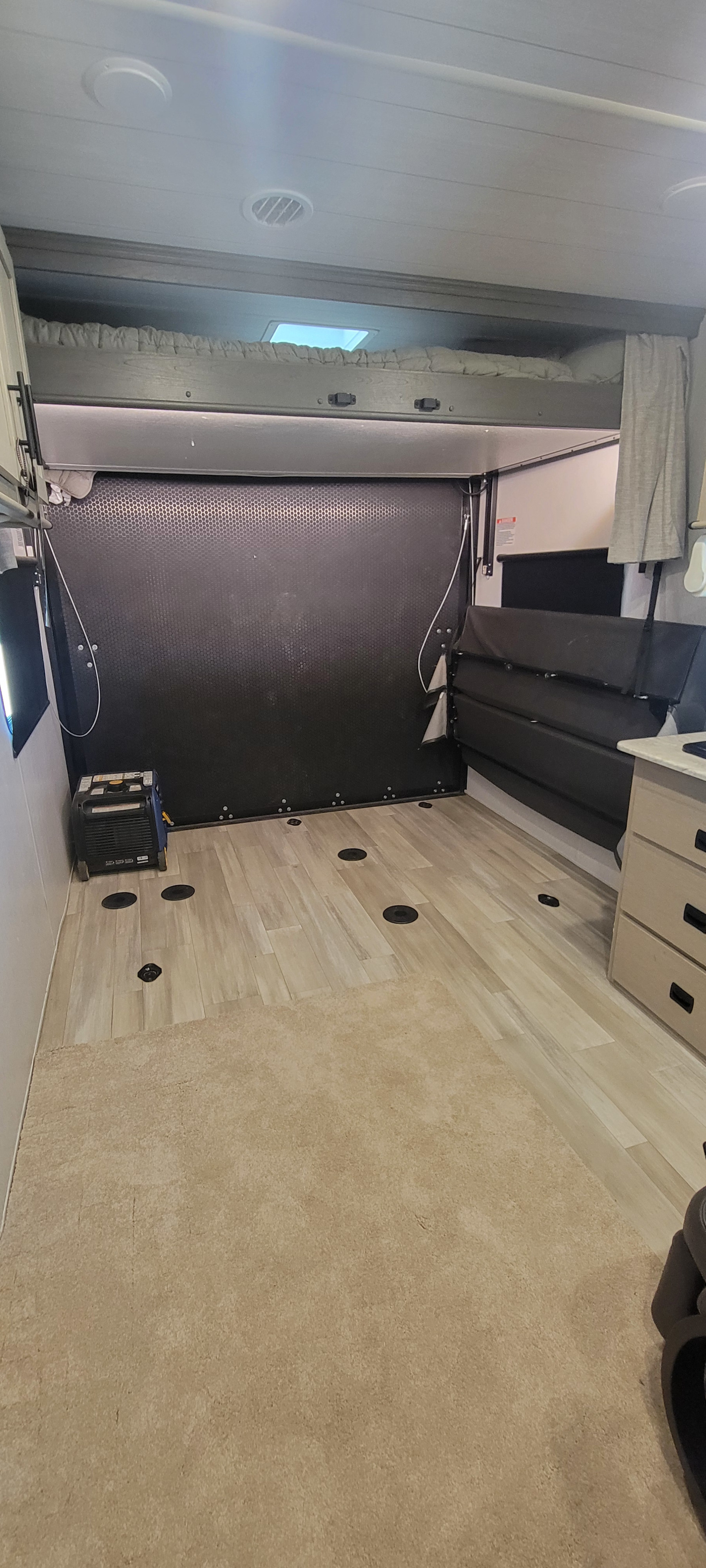 Spacious RV rental toy hauler interior, featuring overhead bunk, fold-up seating, and tie-down flooring for gear.. Forest River Sandstorm 2024