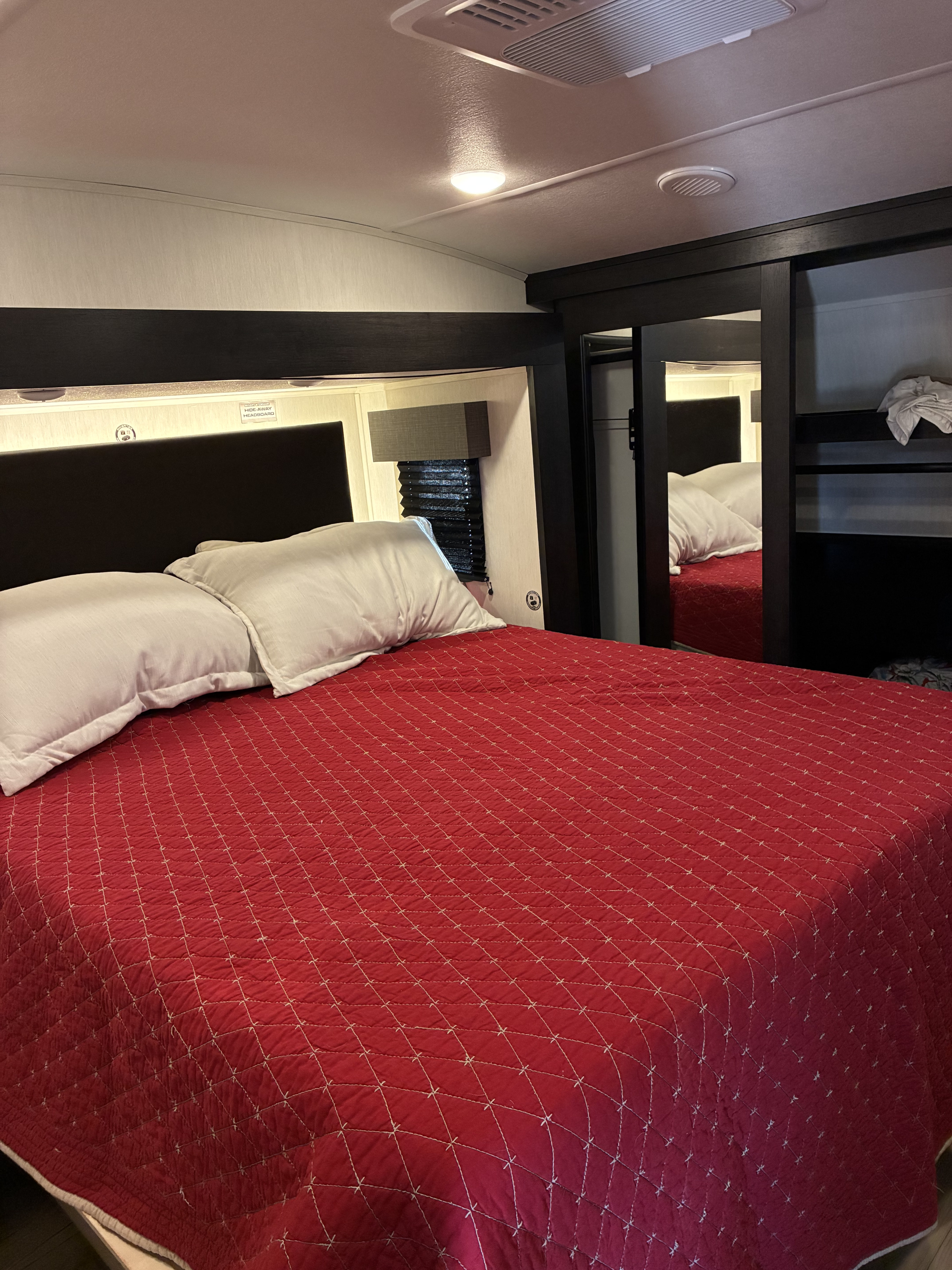 Cozy RV rental bedroom with a red quilted bed, white pillows, integrated lighting, and storage, ideal for travel.. Forest River Sabre 2025