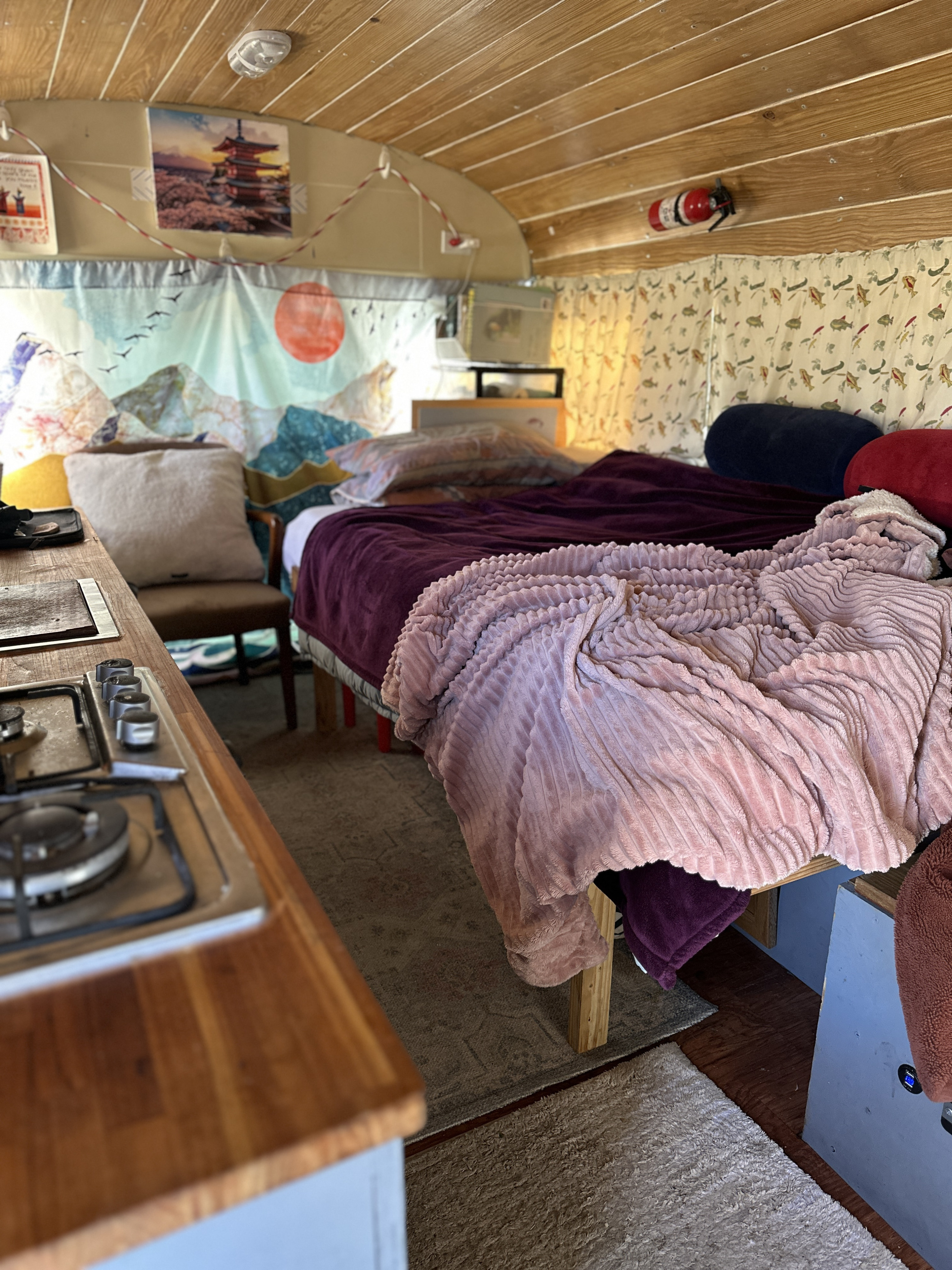 Cozy RV rental interior features a comfortable bed, compact kitchenette, and decorative tapestries, plus essential safety equipment.. GMC Vandura 1986