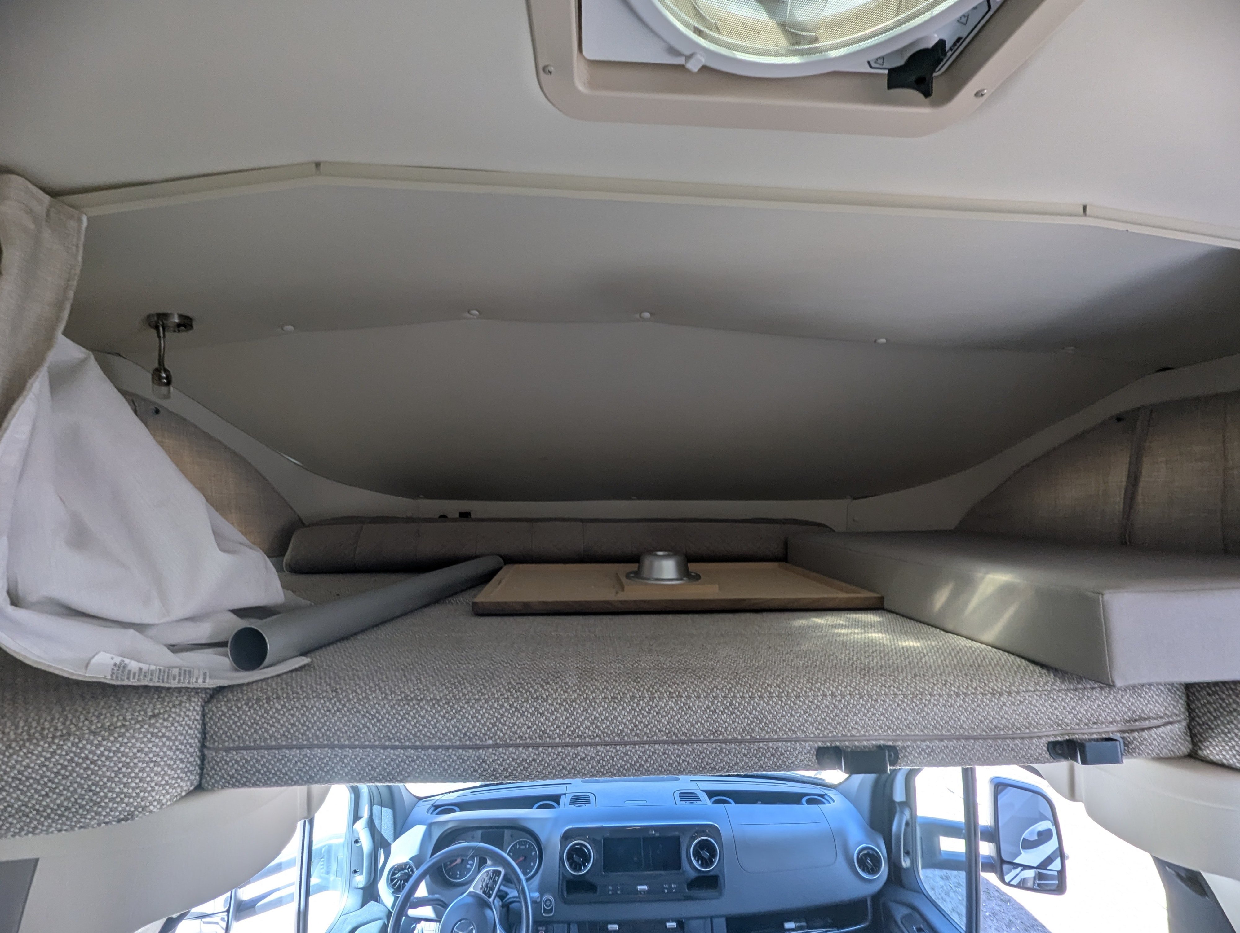 RV rental's cab-over bunk bed overlooking the driver's dashboard and steering wheel, with a ceiling vent above.. Winnebago Navion 2021