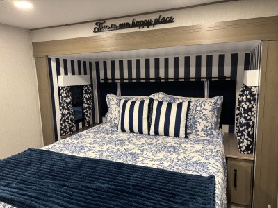 Cozy blue & white RV rental bedroom. Features nautical stripes, toile bedding, and a "happy place" sign above the bed.. Grand Design Reflection 2025