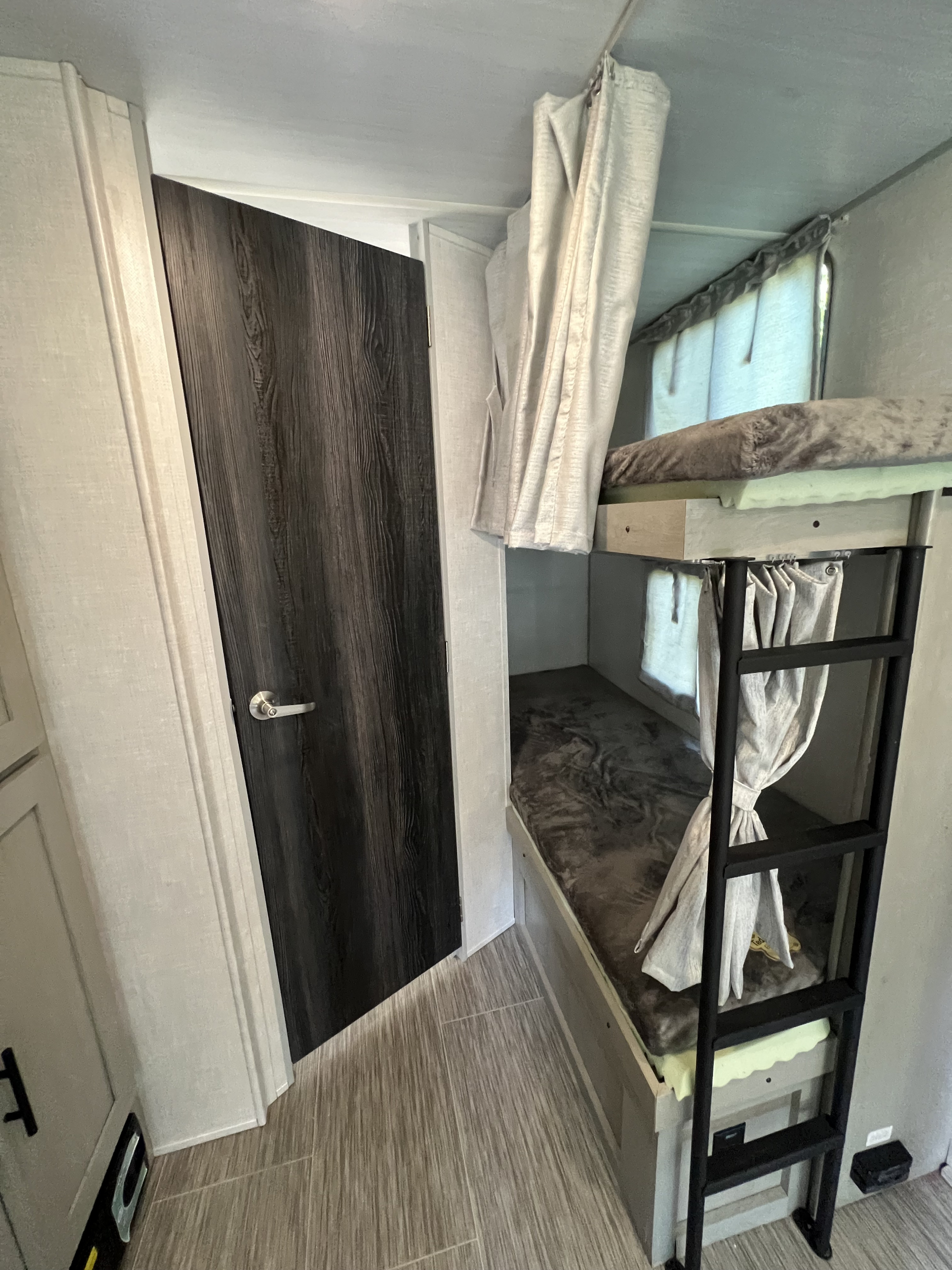 RV rental interior featuring cozy bunk beds with privacy curtains and a ladder, next to a dark wood door.. Forest River Ibex 2021