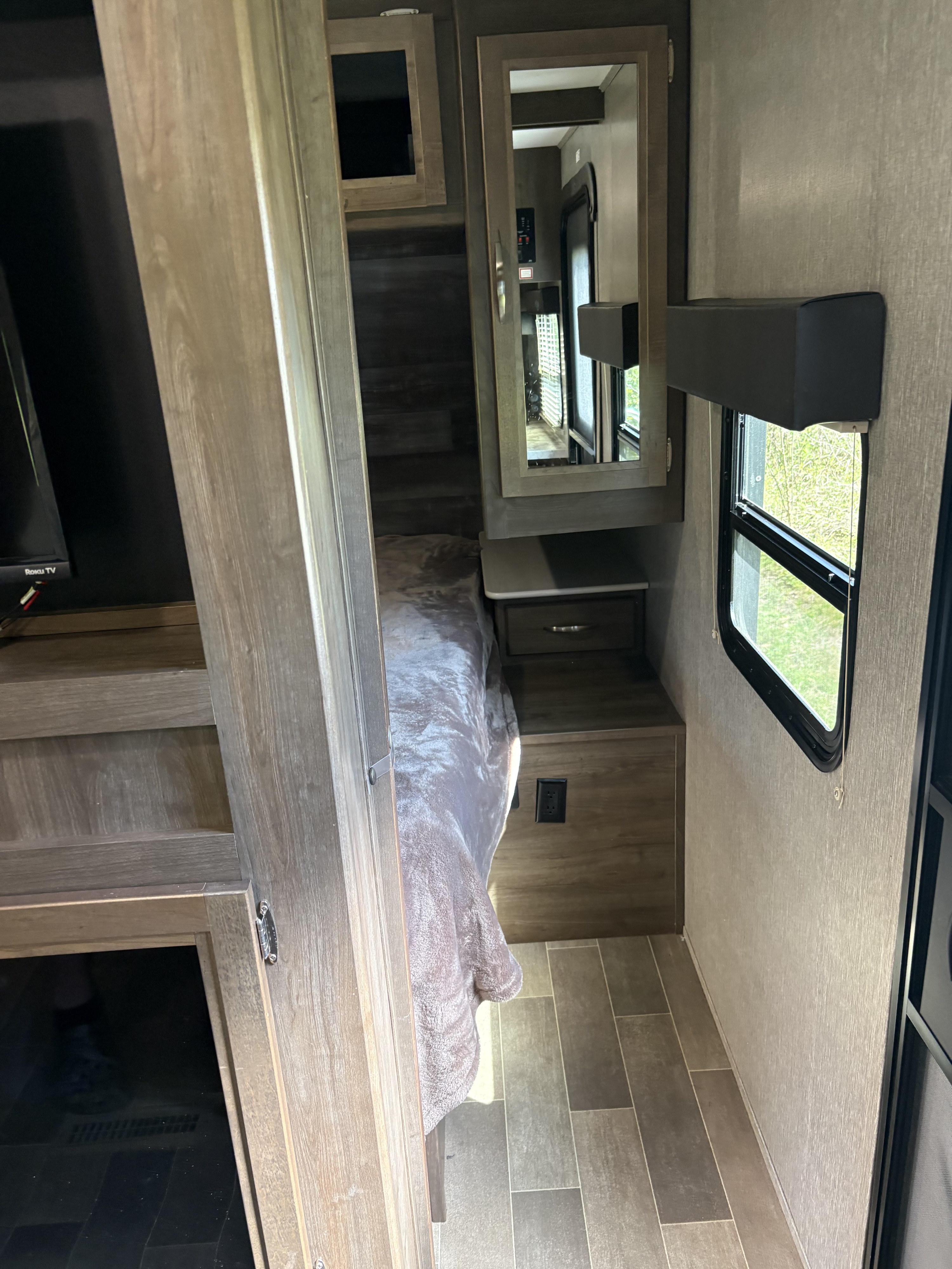 Inside an RV rental: a compact bedroom with a plush bed, mirror, window overlooking nature, and stylish wood paneling.. Dutchmen Coleman Light 2019