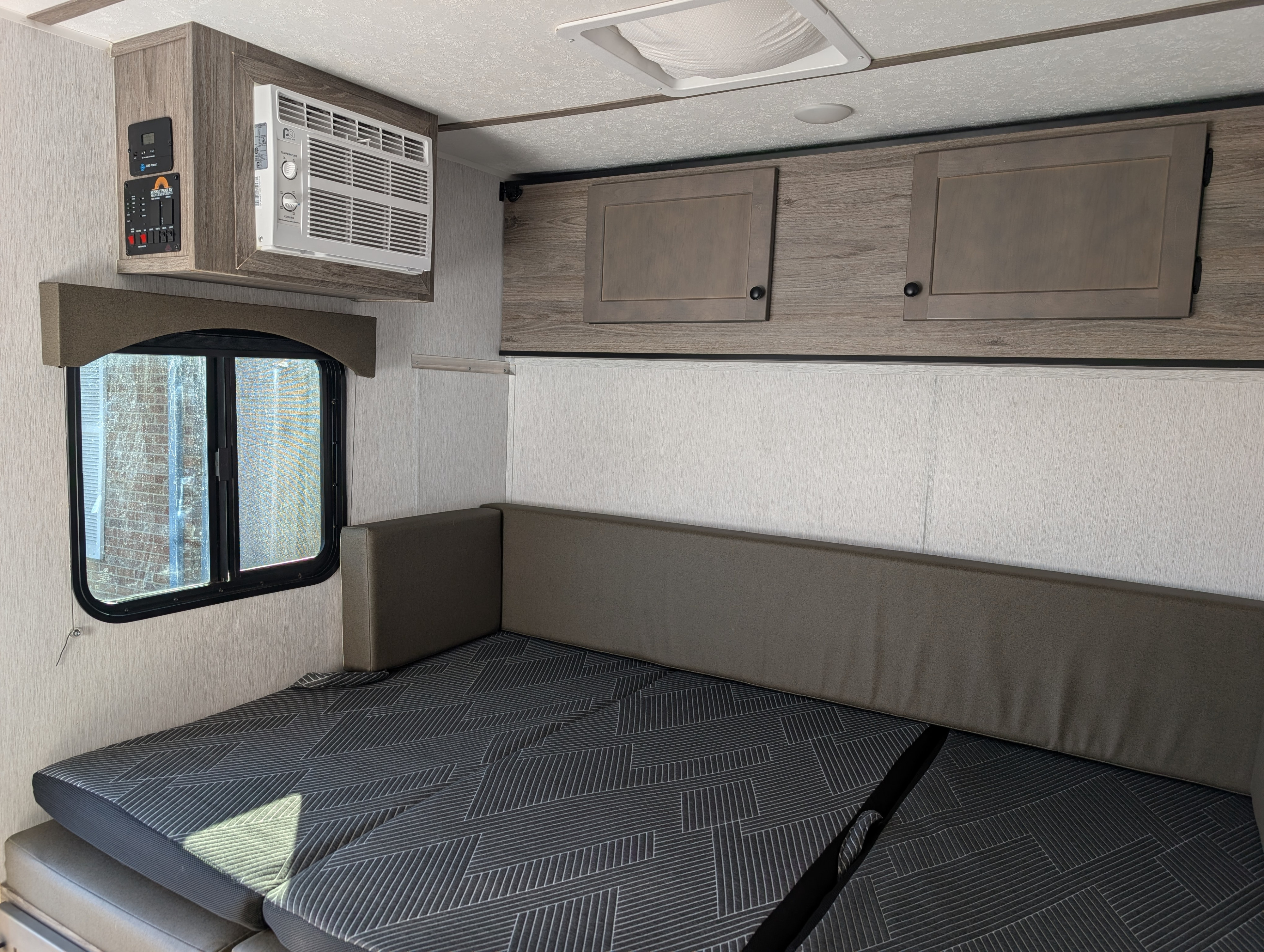 RV rental interior featuring a convertible bed/dinette with patterned cushions, overhead AC, control panel, and cabinets.. Sunset Park RV SunRay 2023