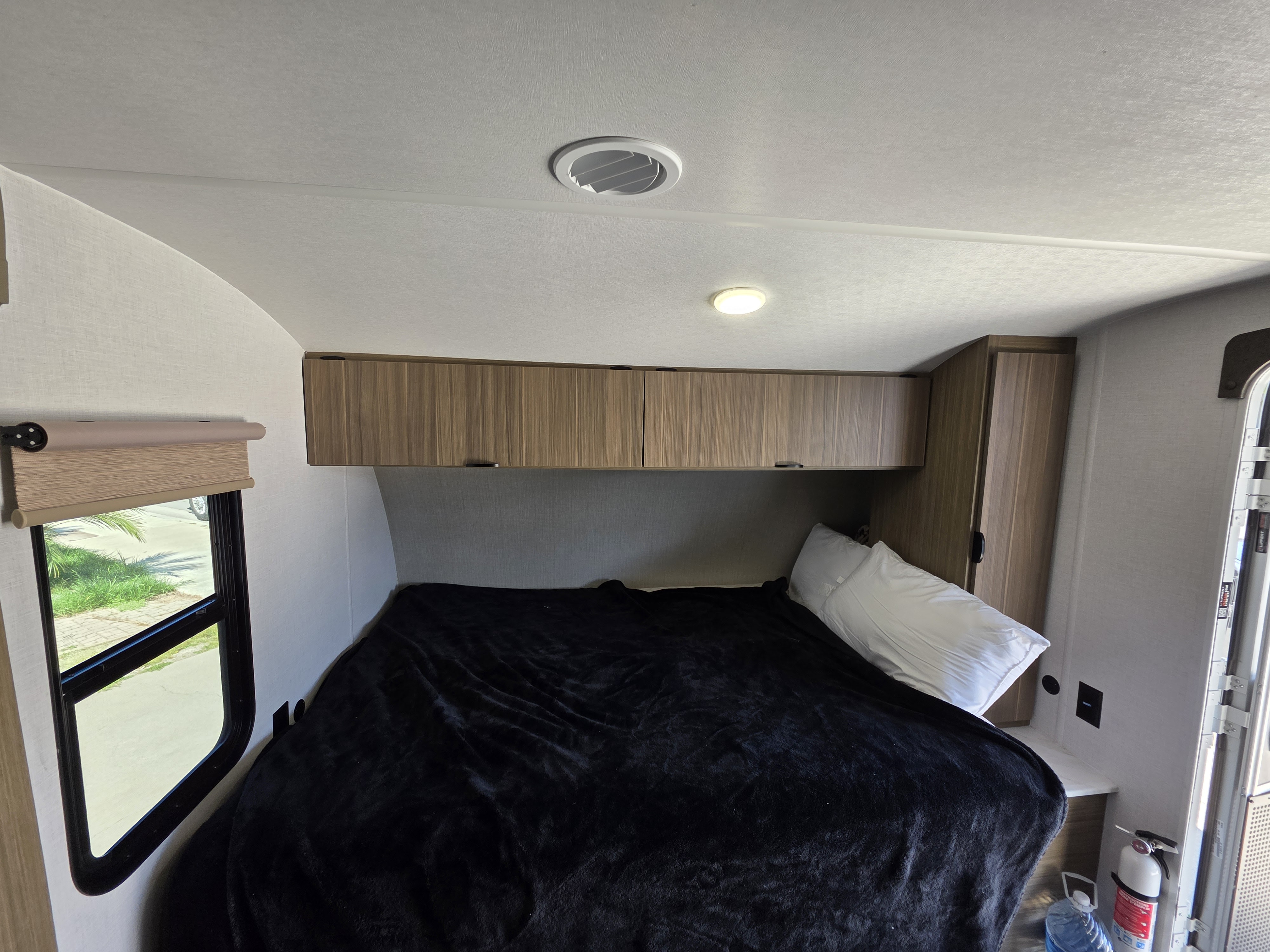 RV rental bedroom showcasing a comfortable bed, wood overhead storage, a window, and ceiling vents for a cozy interior.. Forest River FSX178BHSK 2025