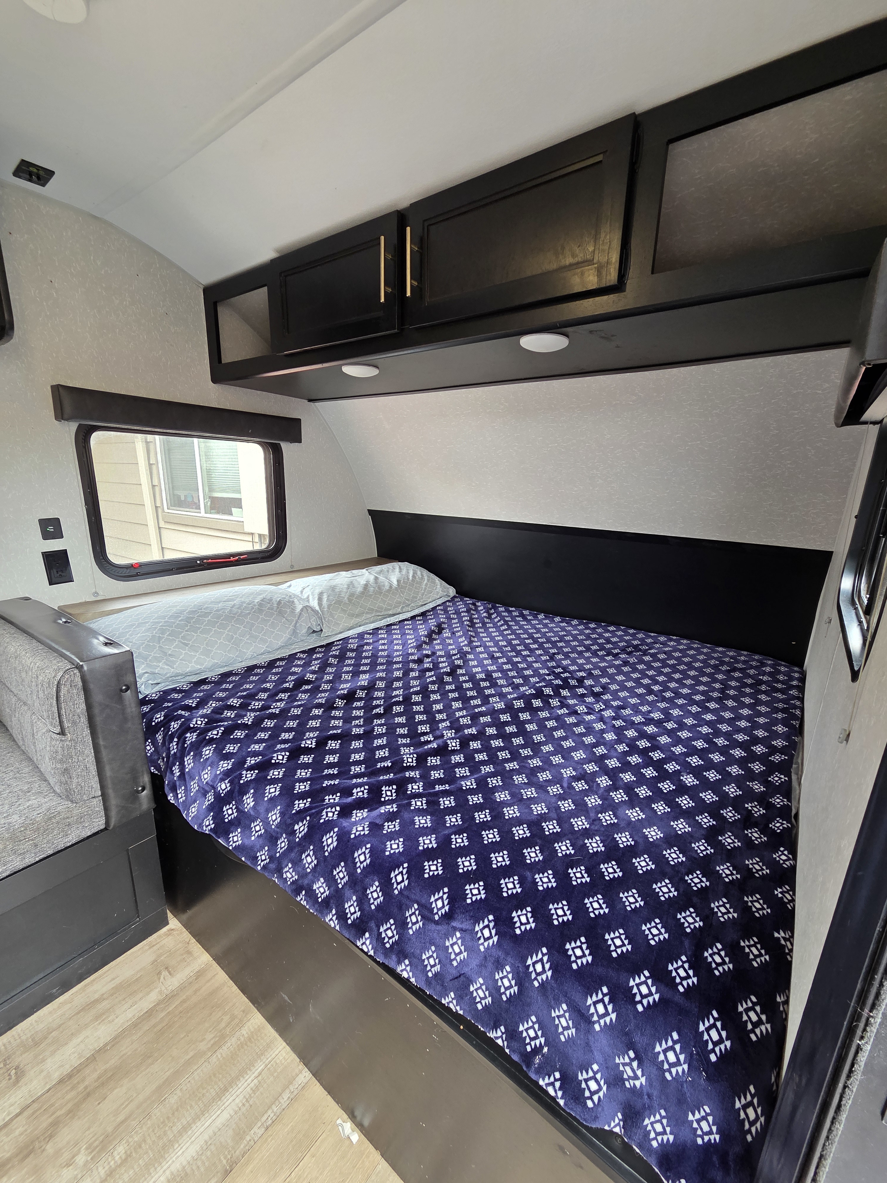 RV rental interior featuring a cozy bedroom with dark cabinets, a window, and a purple patterned bedspread.. Forest River Cherokee Wolf Pup 2022