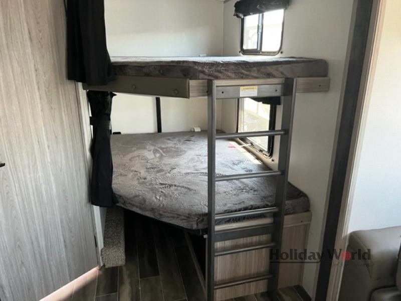 Comfortable RV rental bunk beds, ideal for family travel. Features a ladder, windows, and privacy curtain.. Keystone RV Passport GT 2022