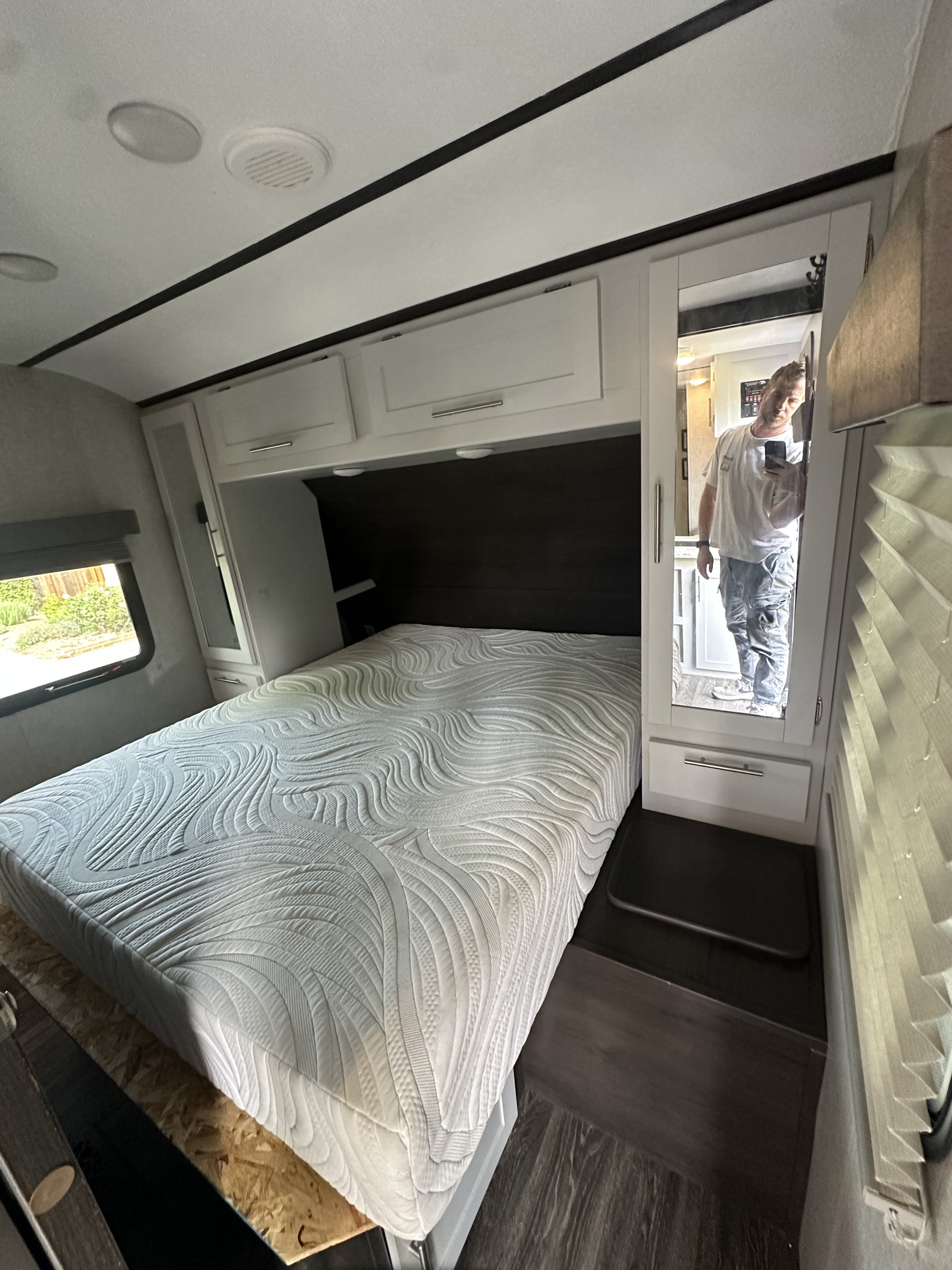 This RV rental bedroom features a comfortable white mattress, overhead storage, and a mirror reflecting the photographer.. Keystone RV Bullet Ultra Lite 2021