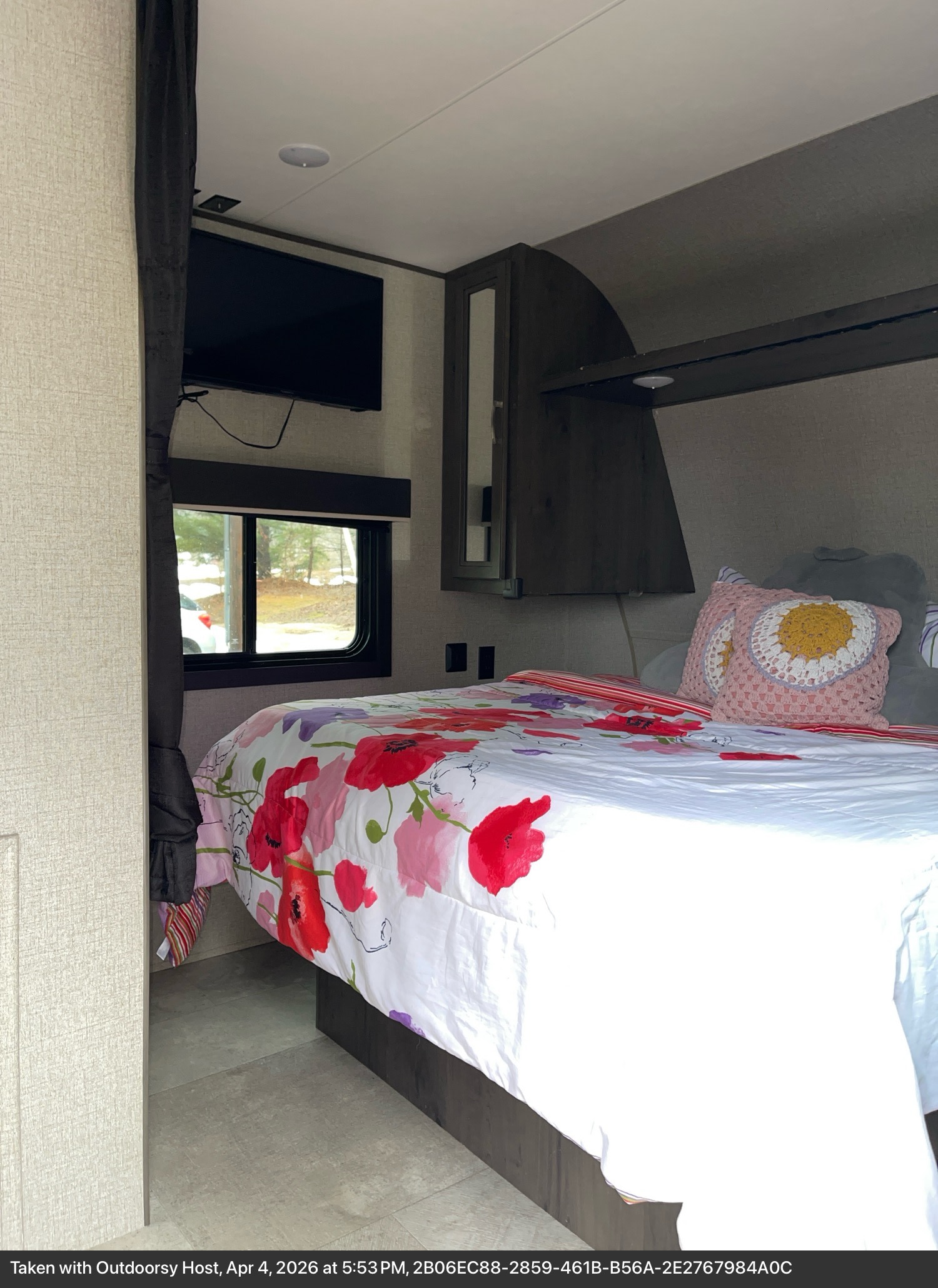 RV rental bedroom interior: cozy bed with floral bedding, wall-mounted TV, window view, and overhead storage.. Jayco Jay Flight SLX 2020
