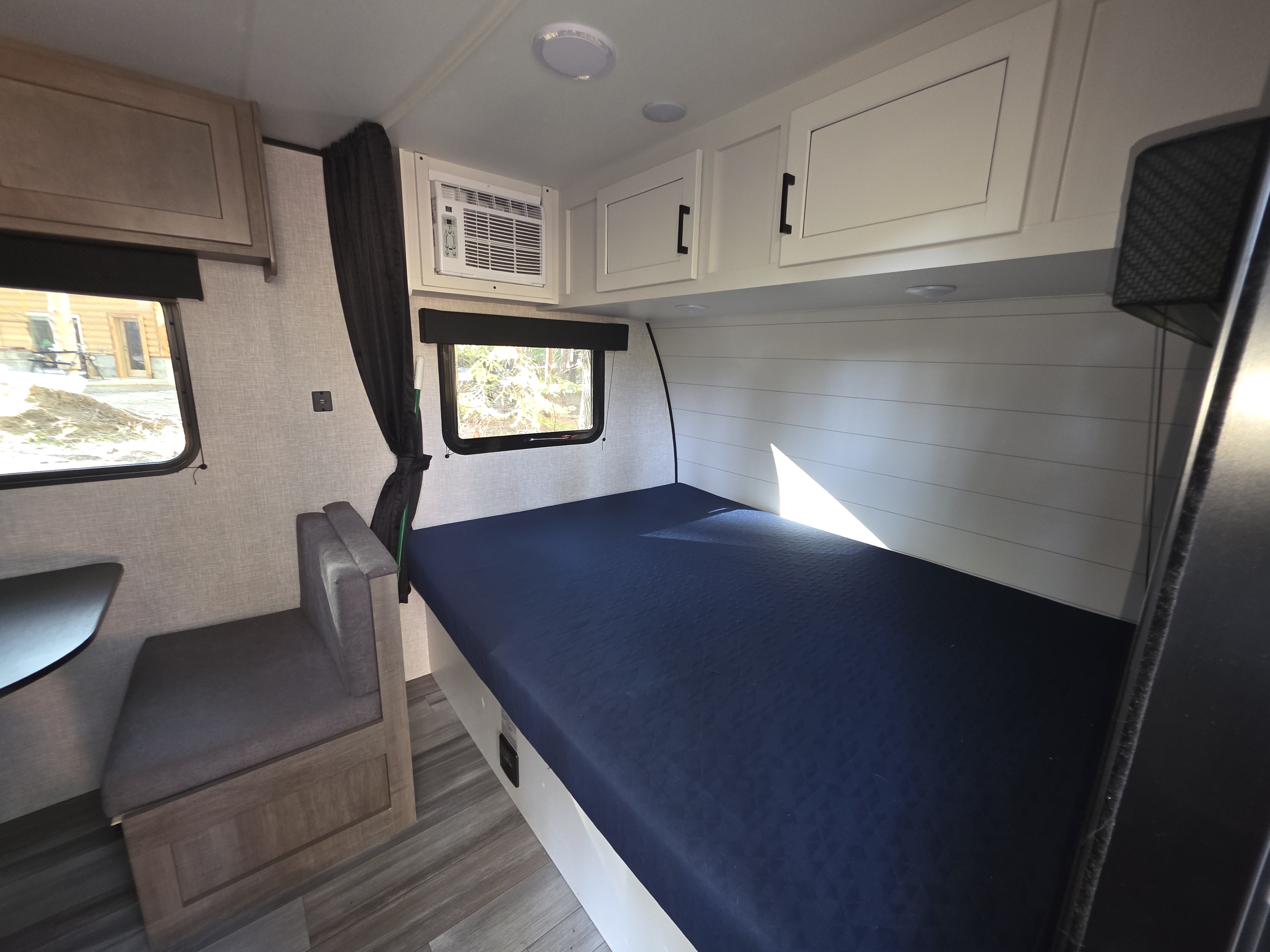 Clean RV rental interior featuring a compact bedroom with blue mattress, white shiplap, AC unit, cabinets, and dinette.. Jayco Jay Flight SLX 2024